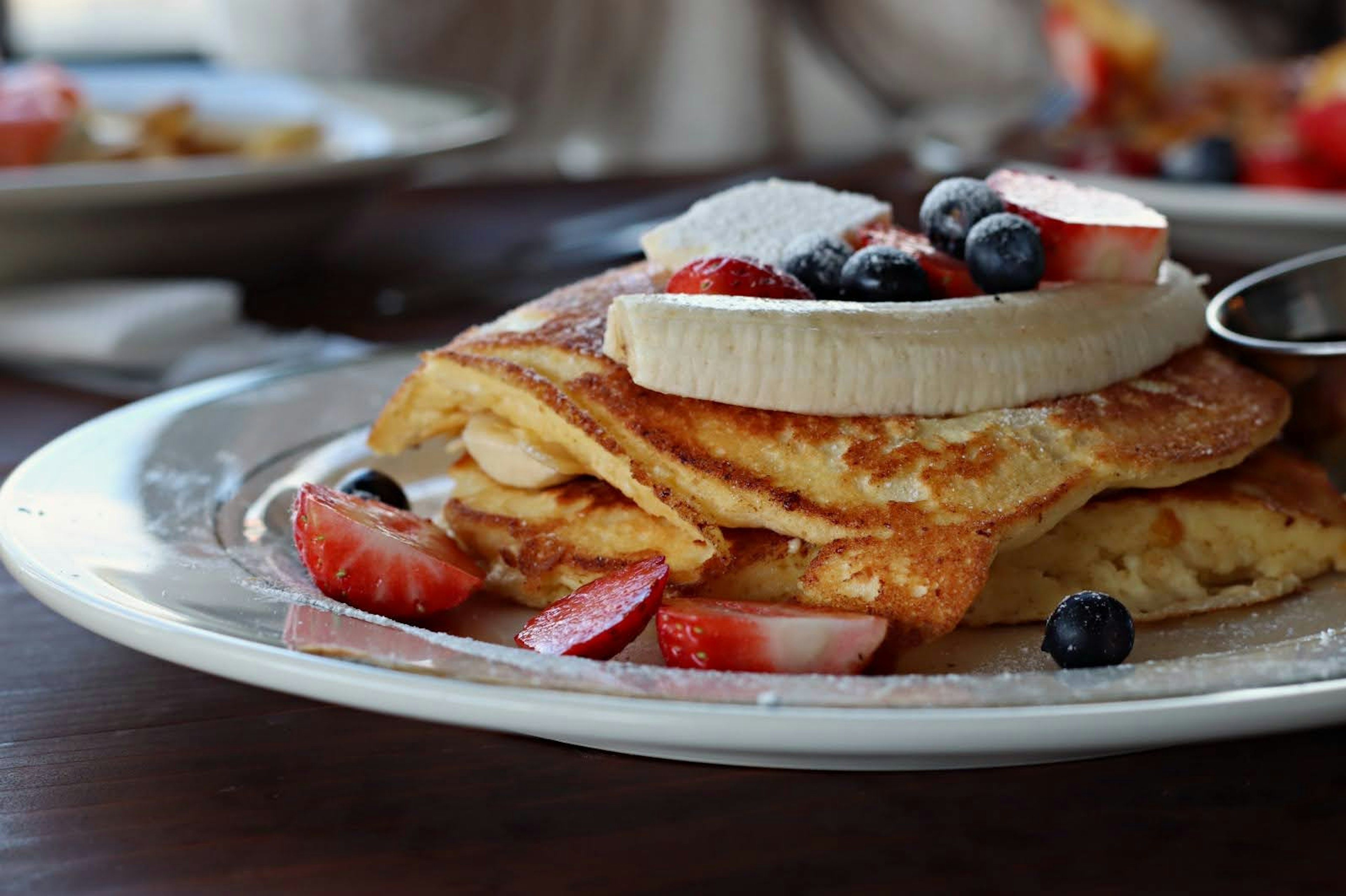 Pancake lembut dengan topping pisang dan beri campuran di atas piring