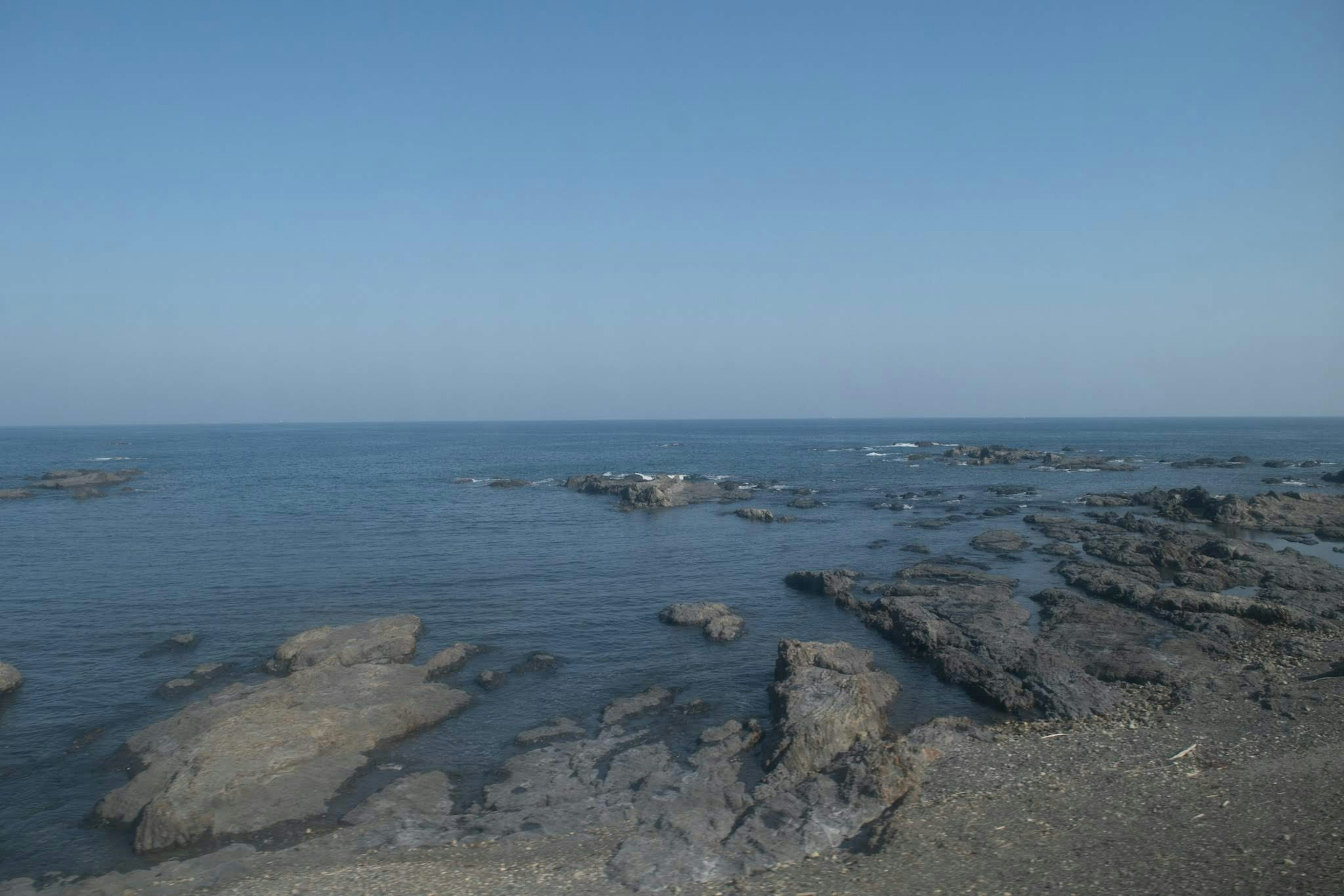 Scenic view of rocky shore and calm sea under blue sky