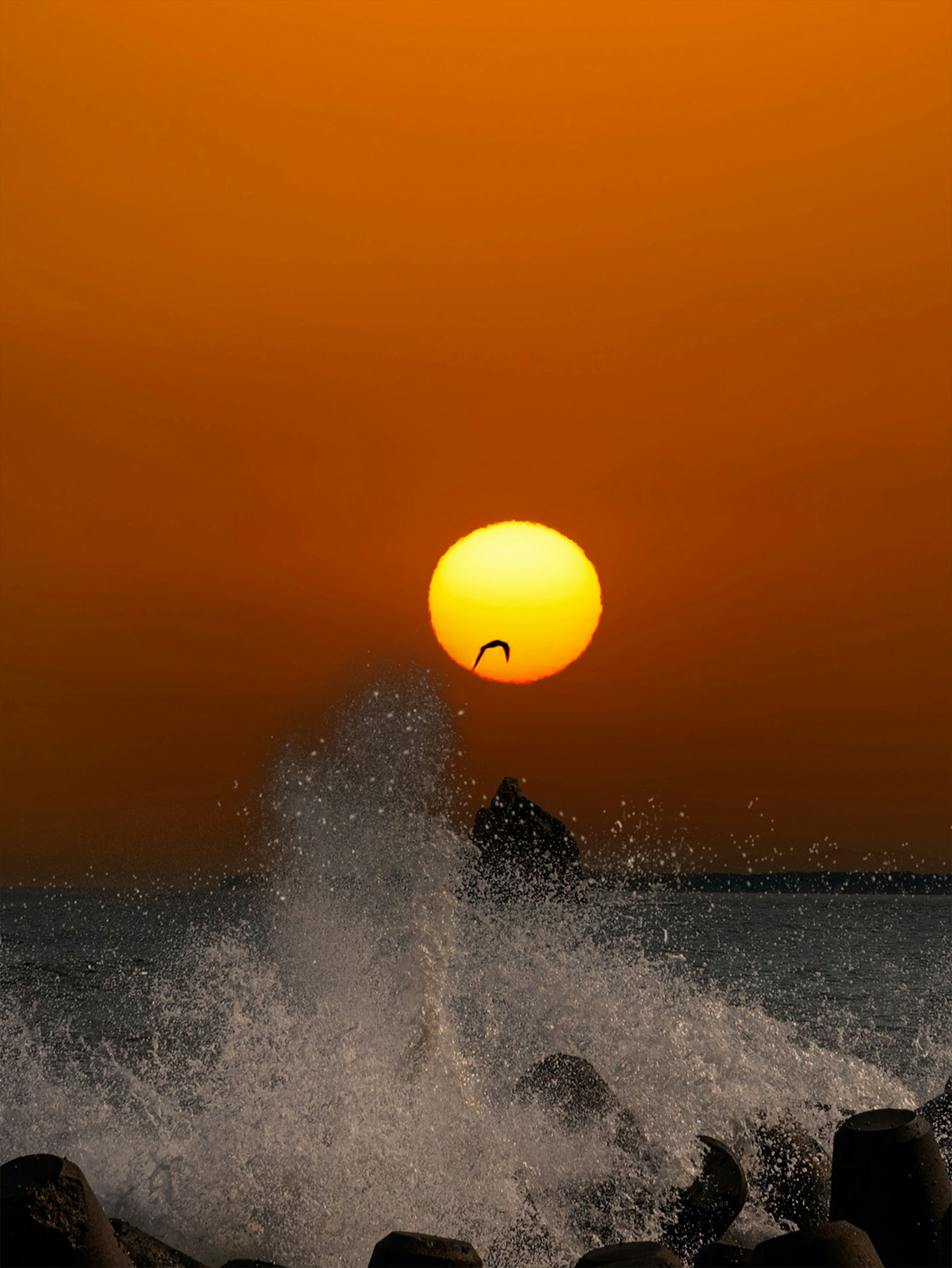 夕日が海面に沈む瞬間と波の飛沫