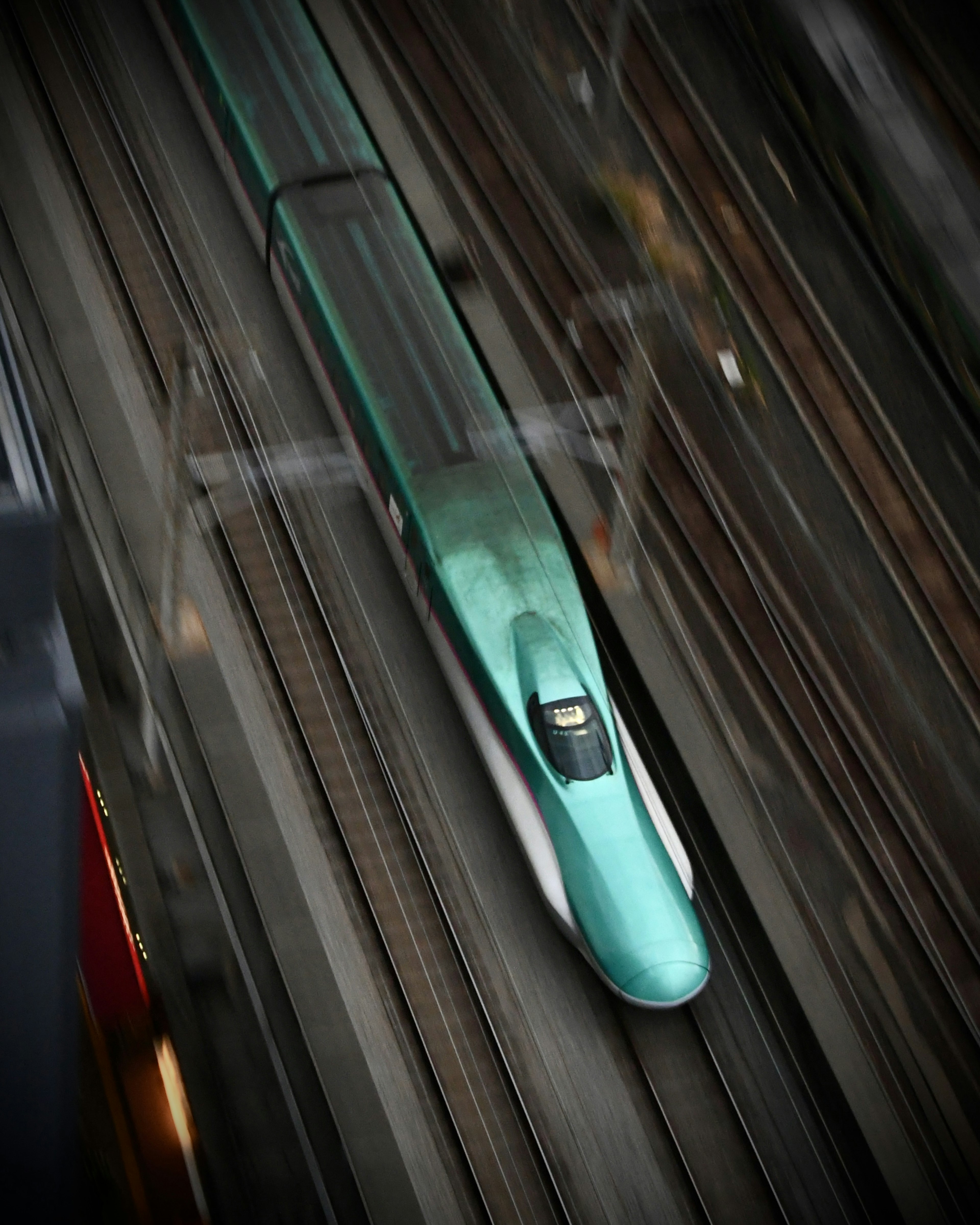 A green Shinkansen train speeding on tracks