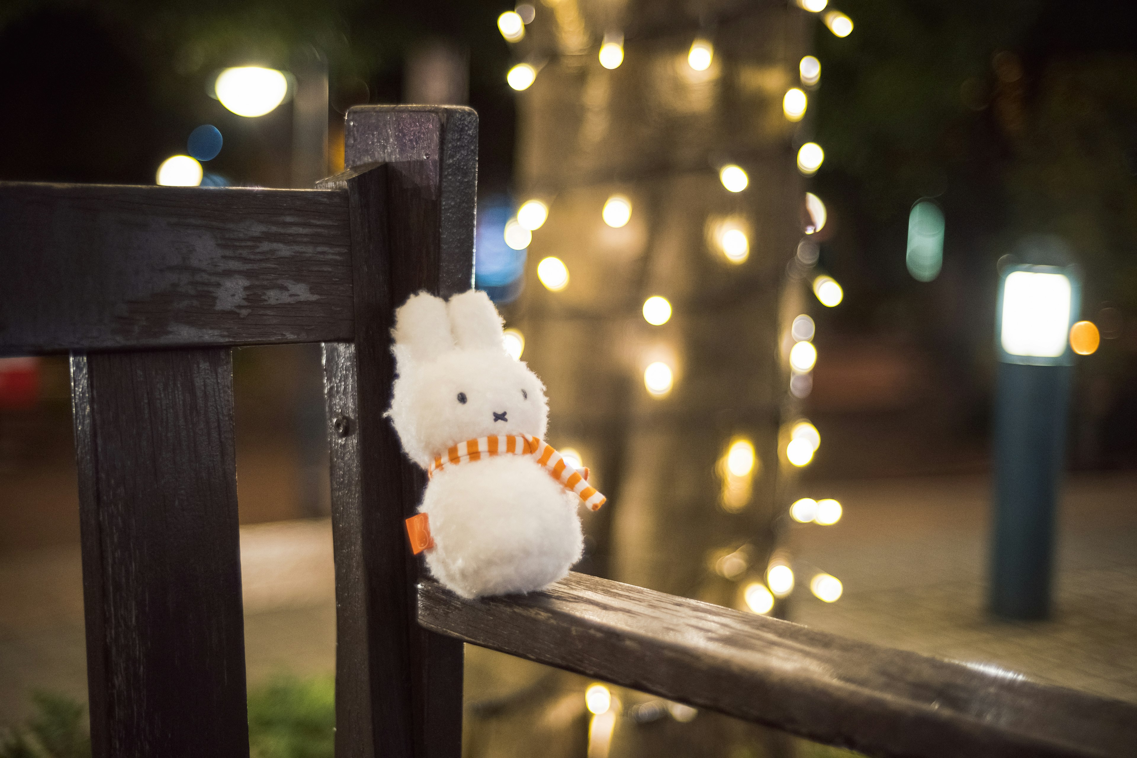 Un giocattolo di peluche bianco a forma di coniglio seduto su una panchina di legno in un parco di notte