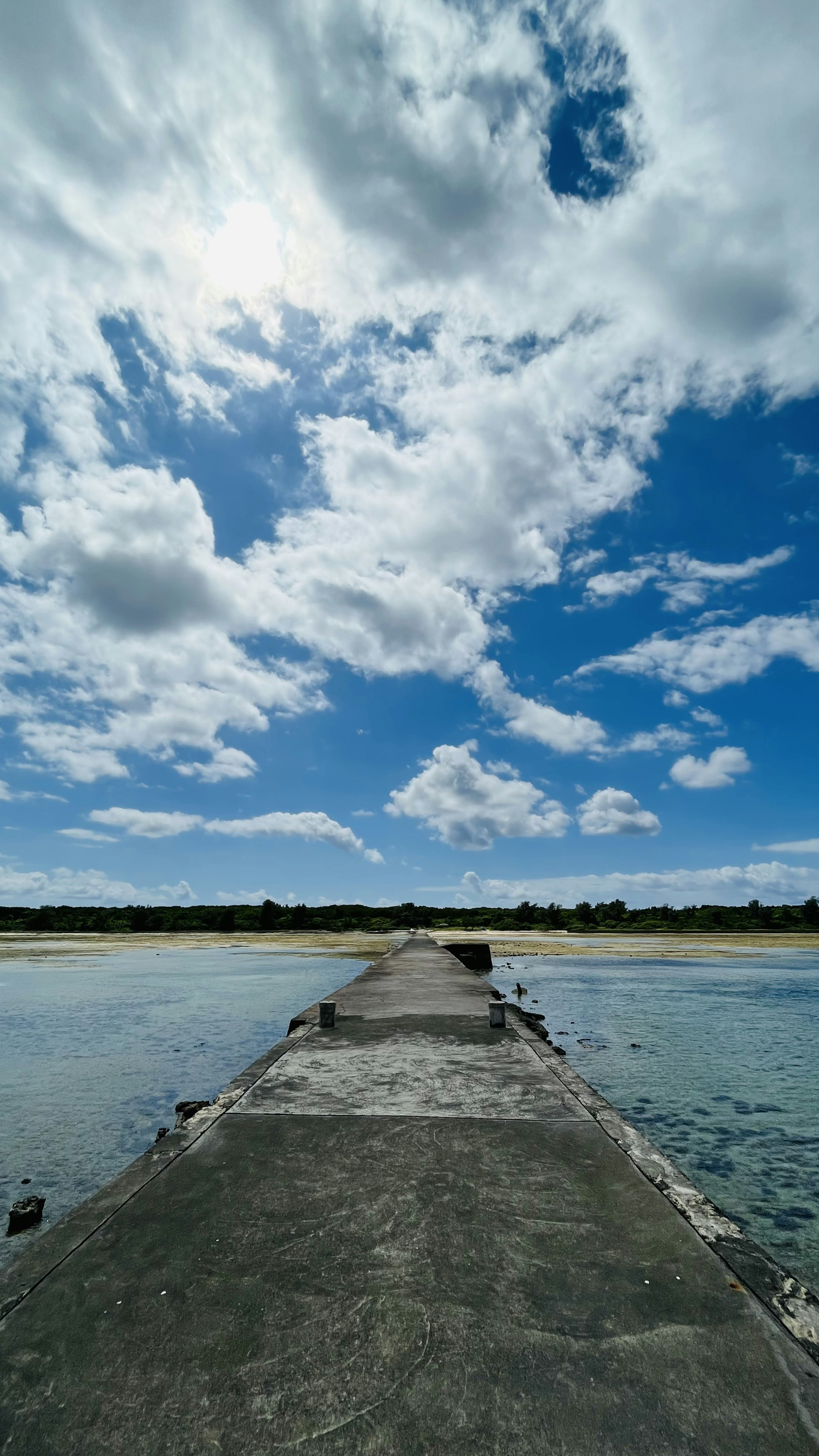 Quai en béton s'étendant dans l'eau sous un ciel bleu clair avec des nuages blancs duveteux