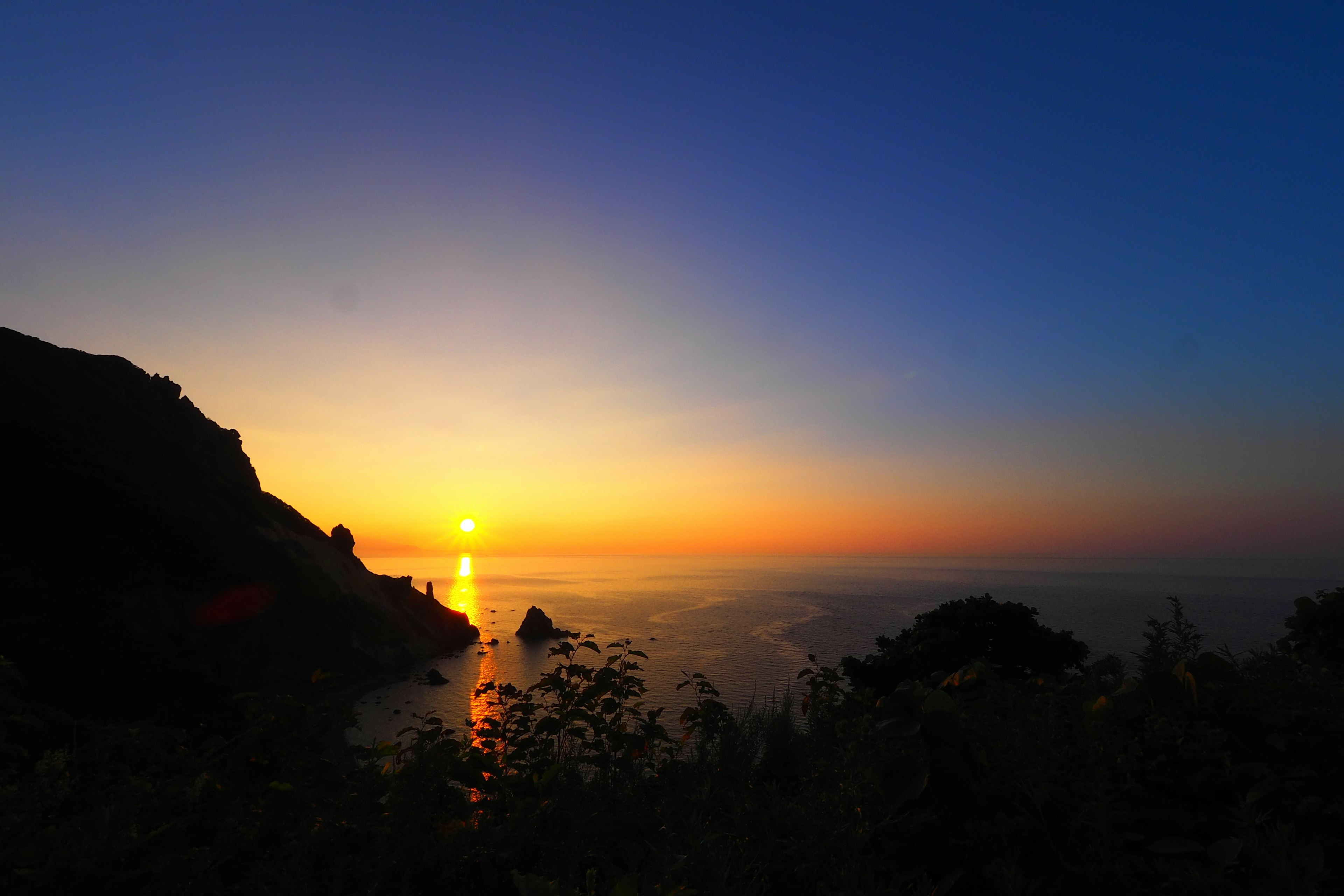 Stunning landscape of sunset over the ocean with deep blue sky and orange reflections