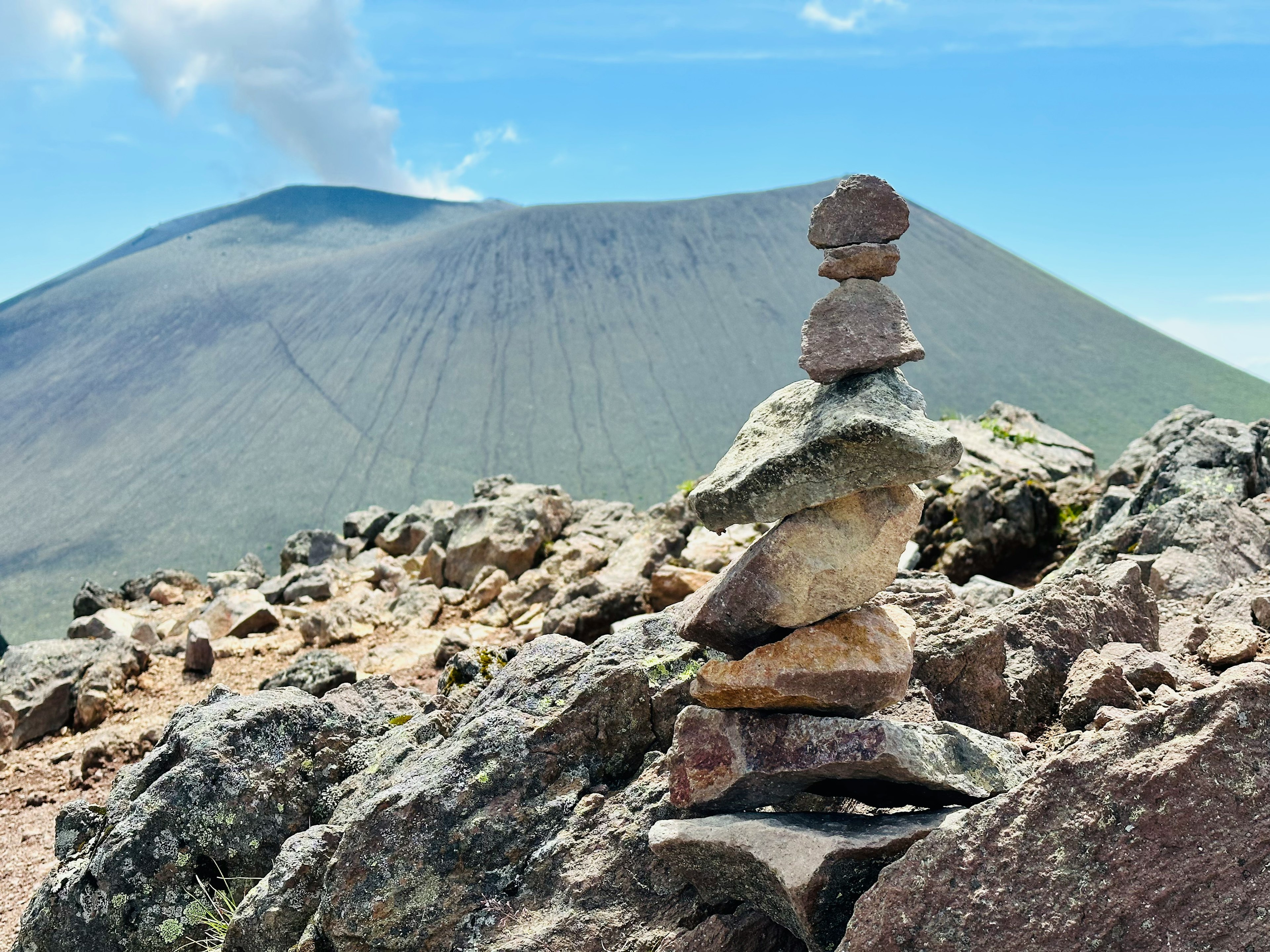 Torre de piedras apiladas en terreno rocoso con un volcán al fondo