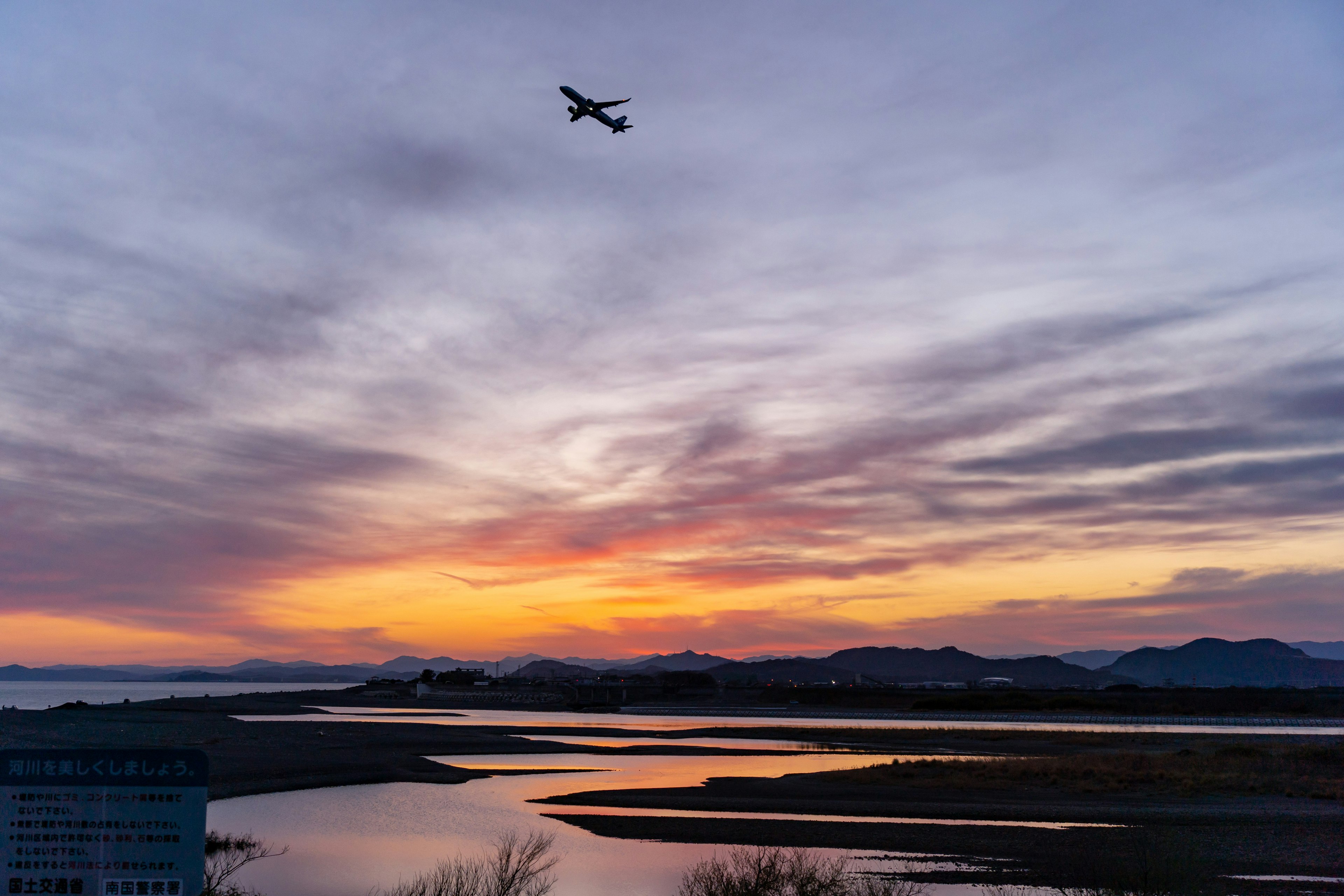 夕焼けの空に飛ぶ小型飛行機と川の景色