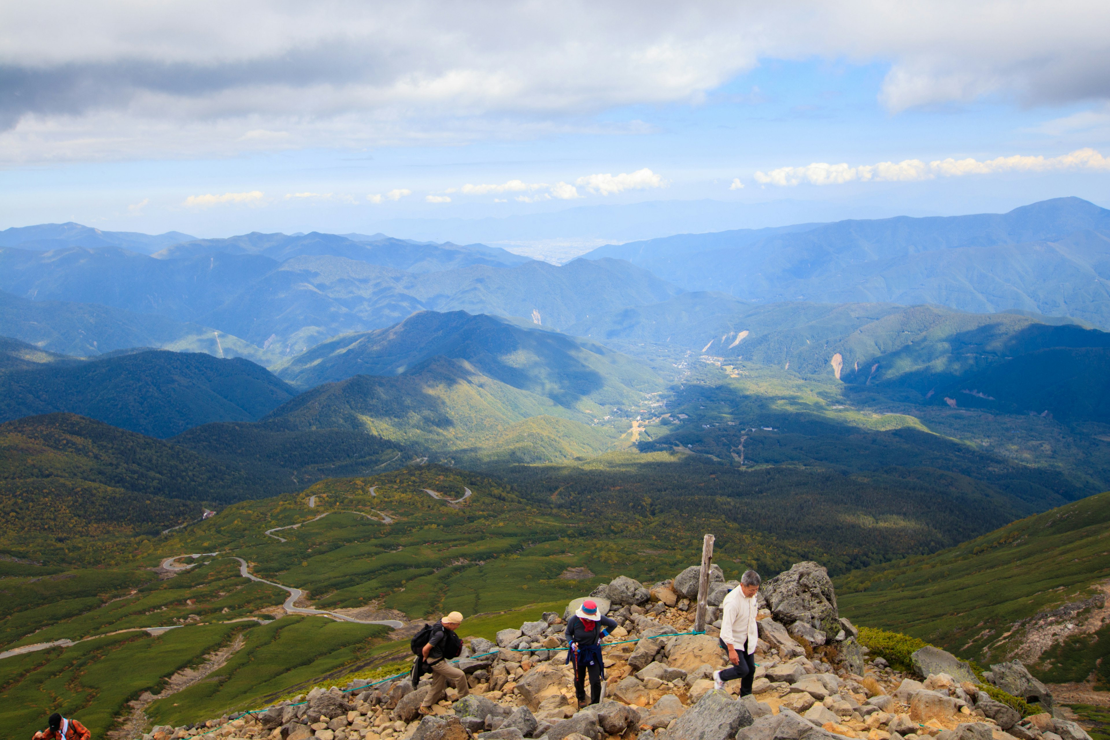 Hikers on a rocky mountain trail with a panoramic view of green valleys