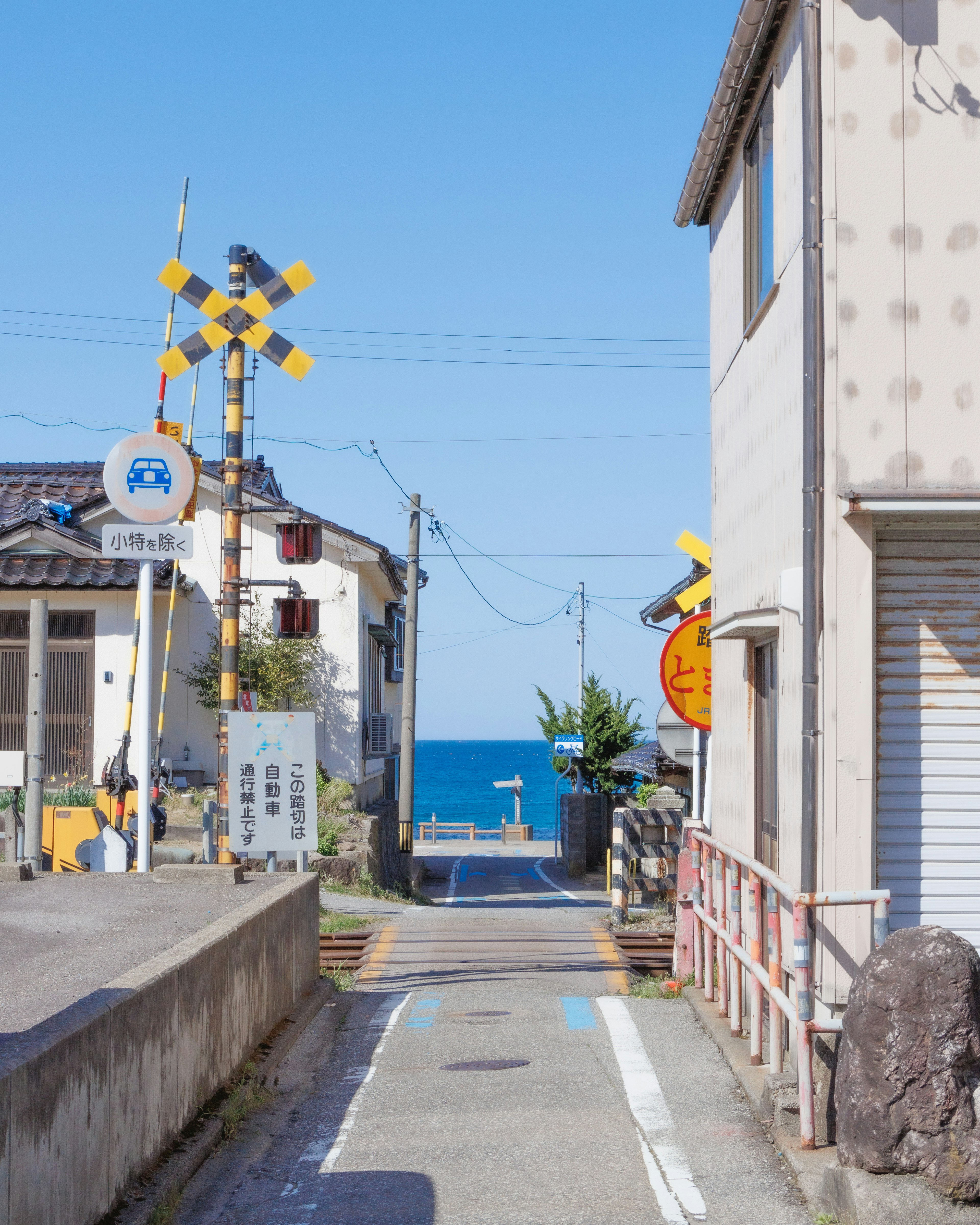 Vista di una strada con mare blu chiaro e segnale di attraversamento ferroviario