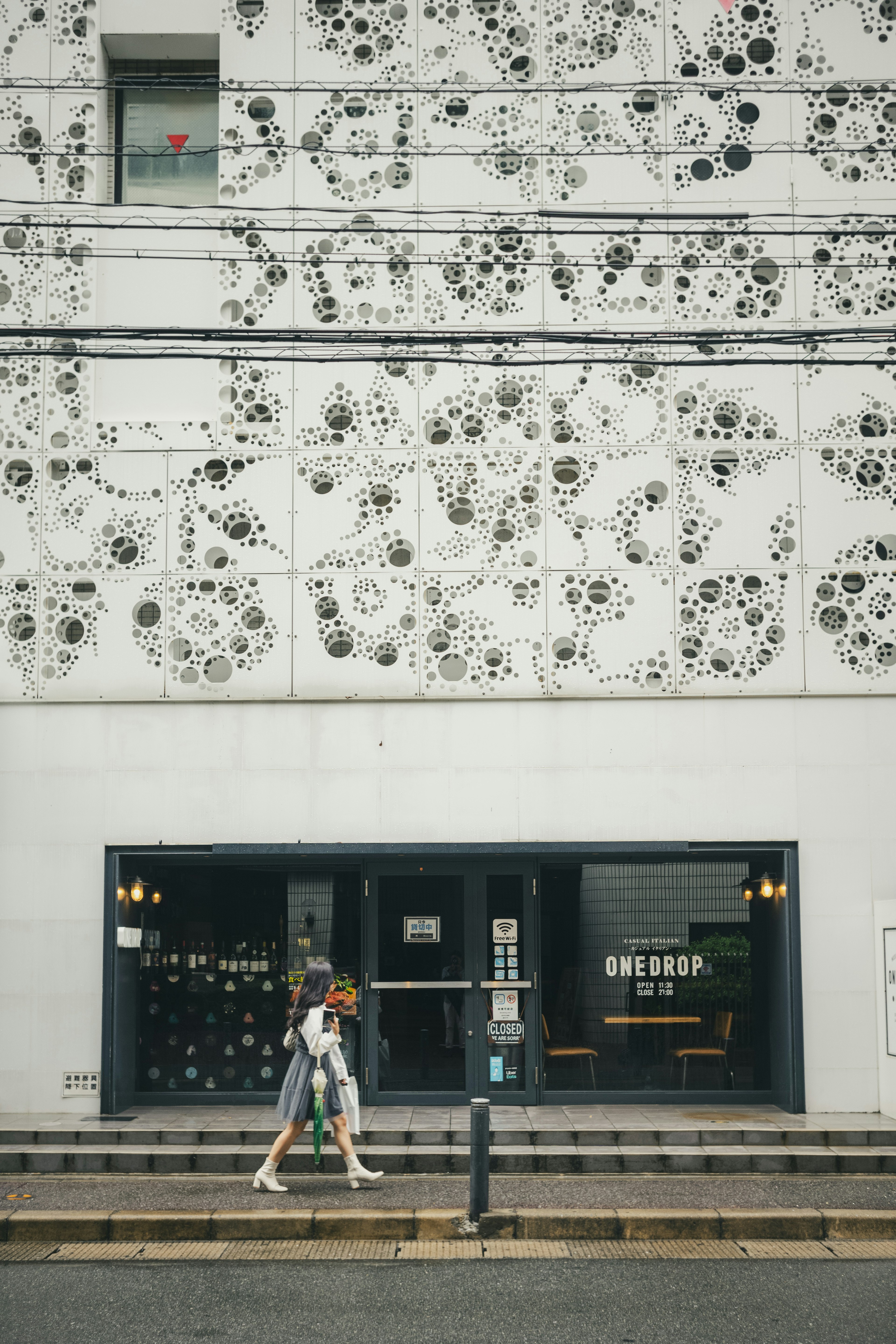 Mujer caminando frente a un edificio con una pared blanca decorativa de agujeros