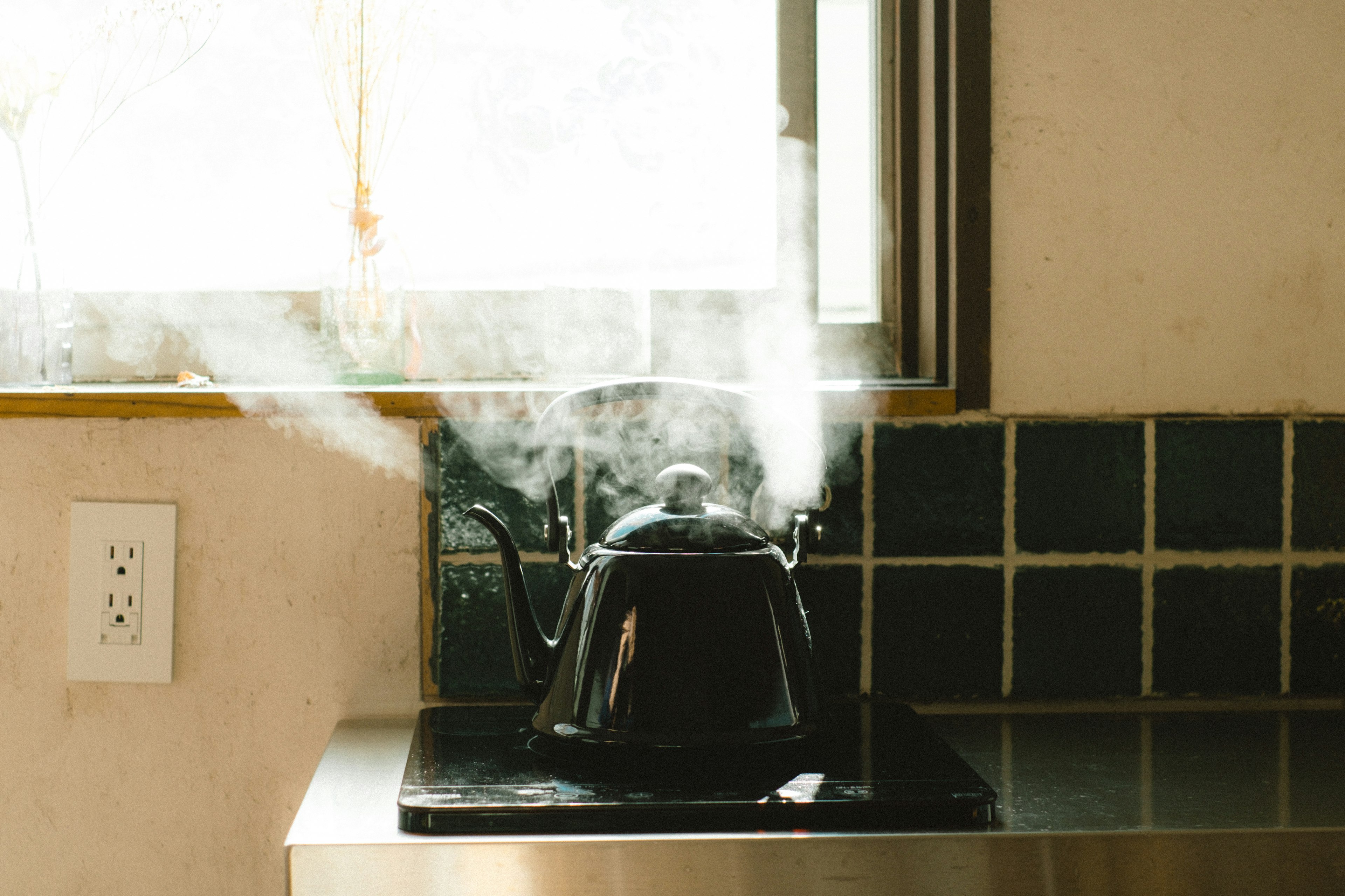 Hervidor negro emitiendo vapor en la encimera de la cocina cerca de una ventana