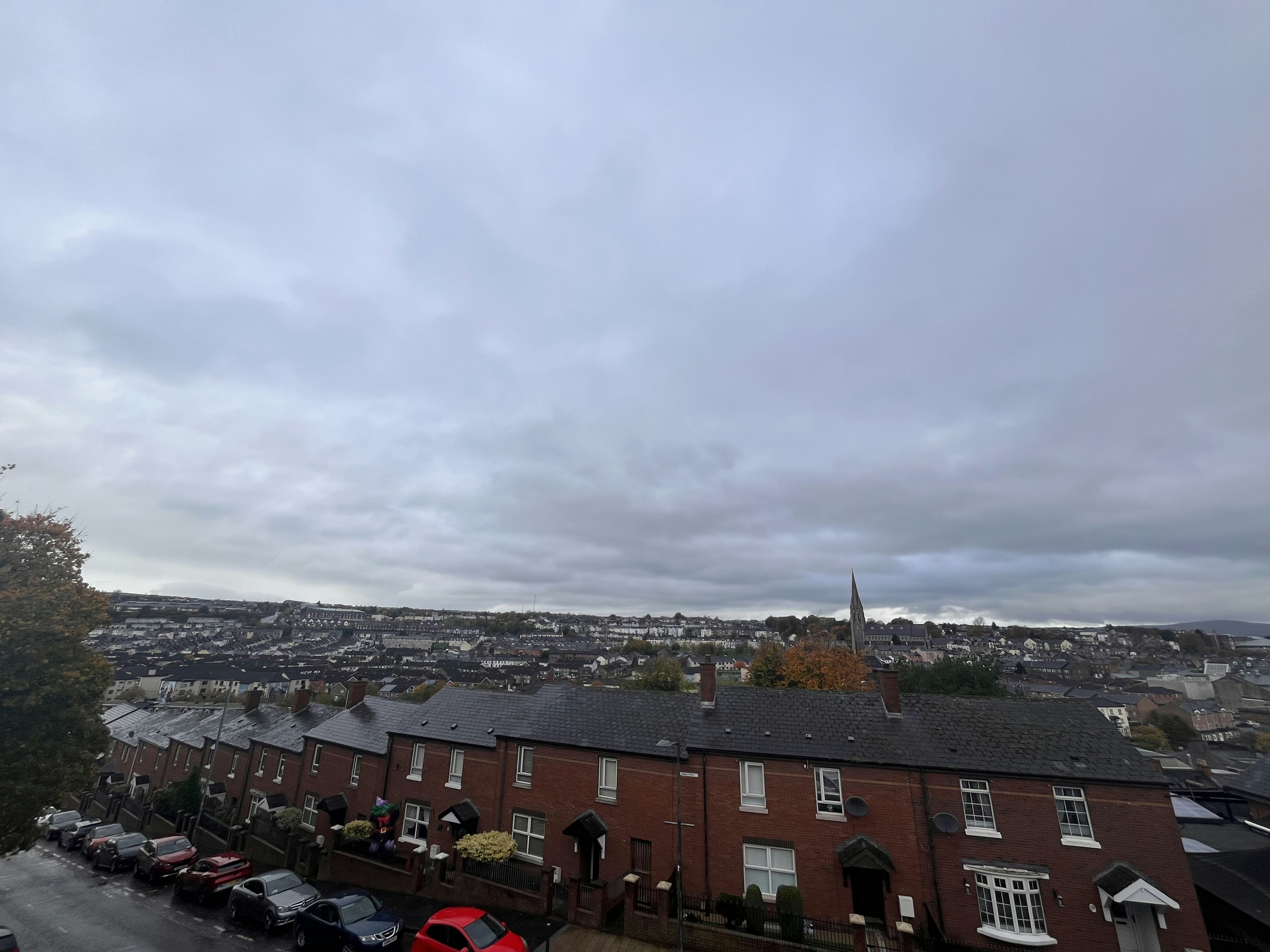 Vue d'une zone résidentielle sous un ciel nuageux avec des toits et des collines au loin