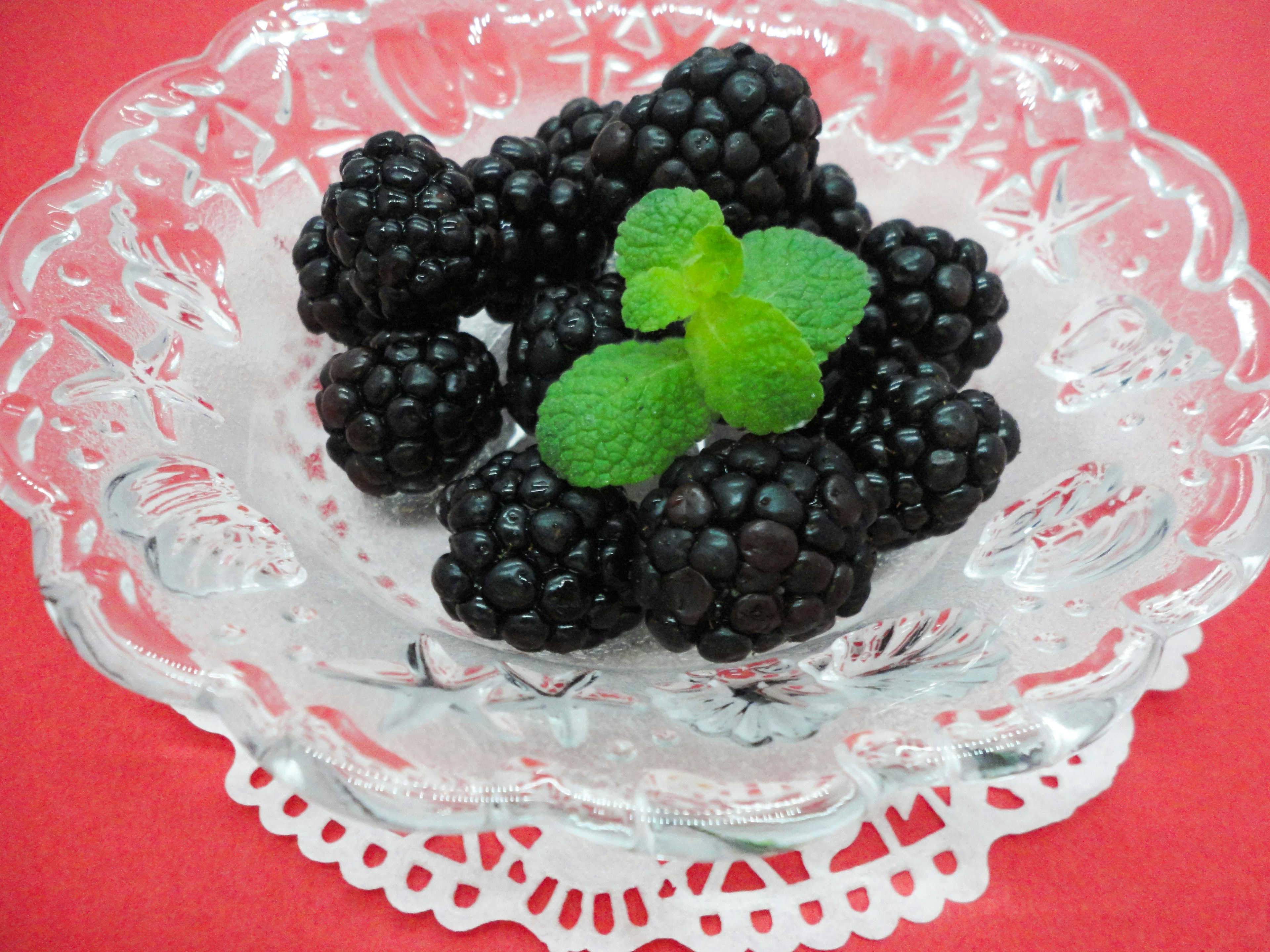 A clear plate with blackberries and mint leaves on a red background