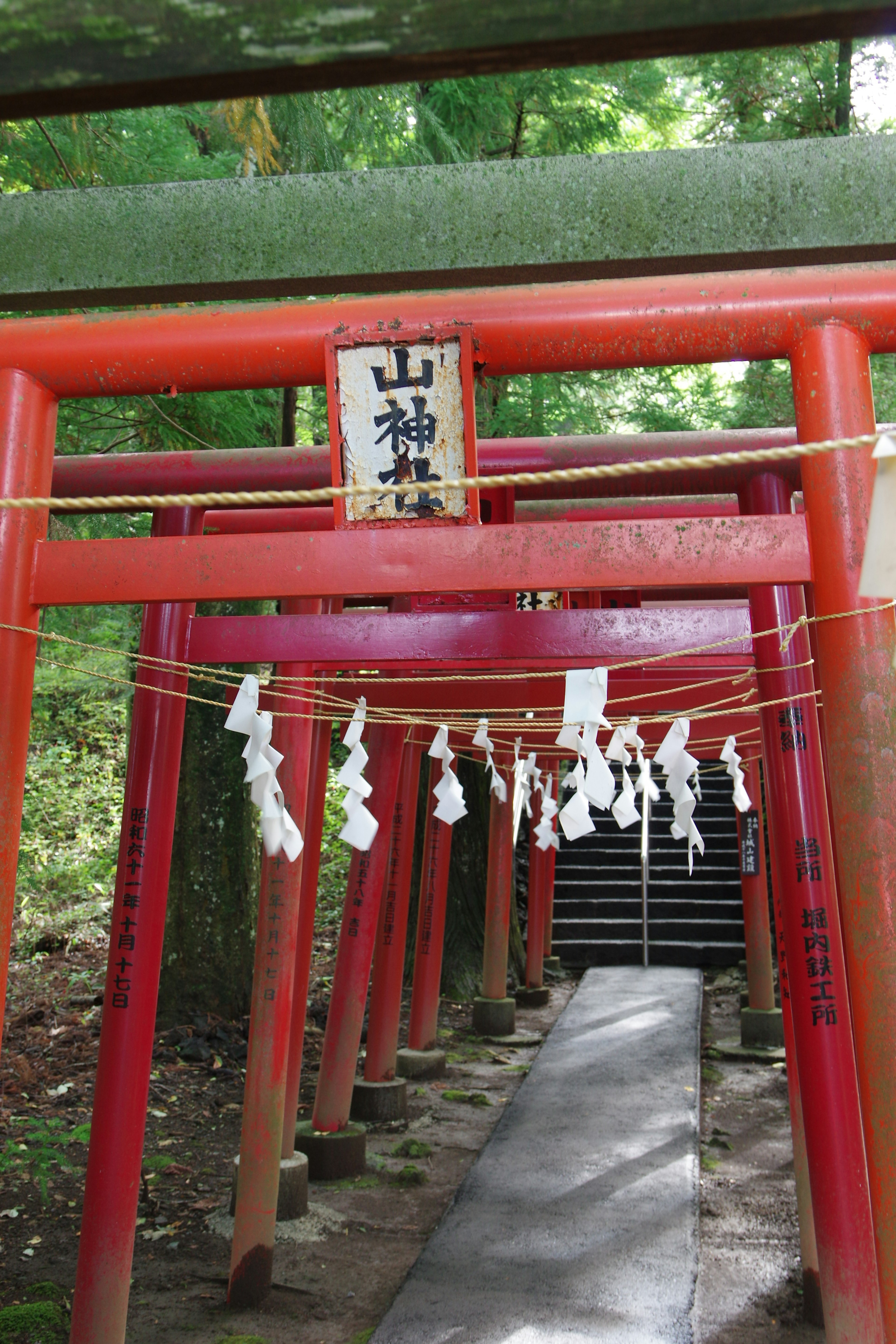 Entrée d'un sanctuaire avec des torii rouges et un panneau avec des omamori blancs