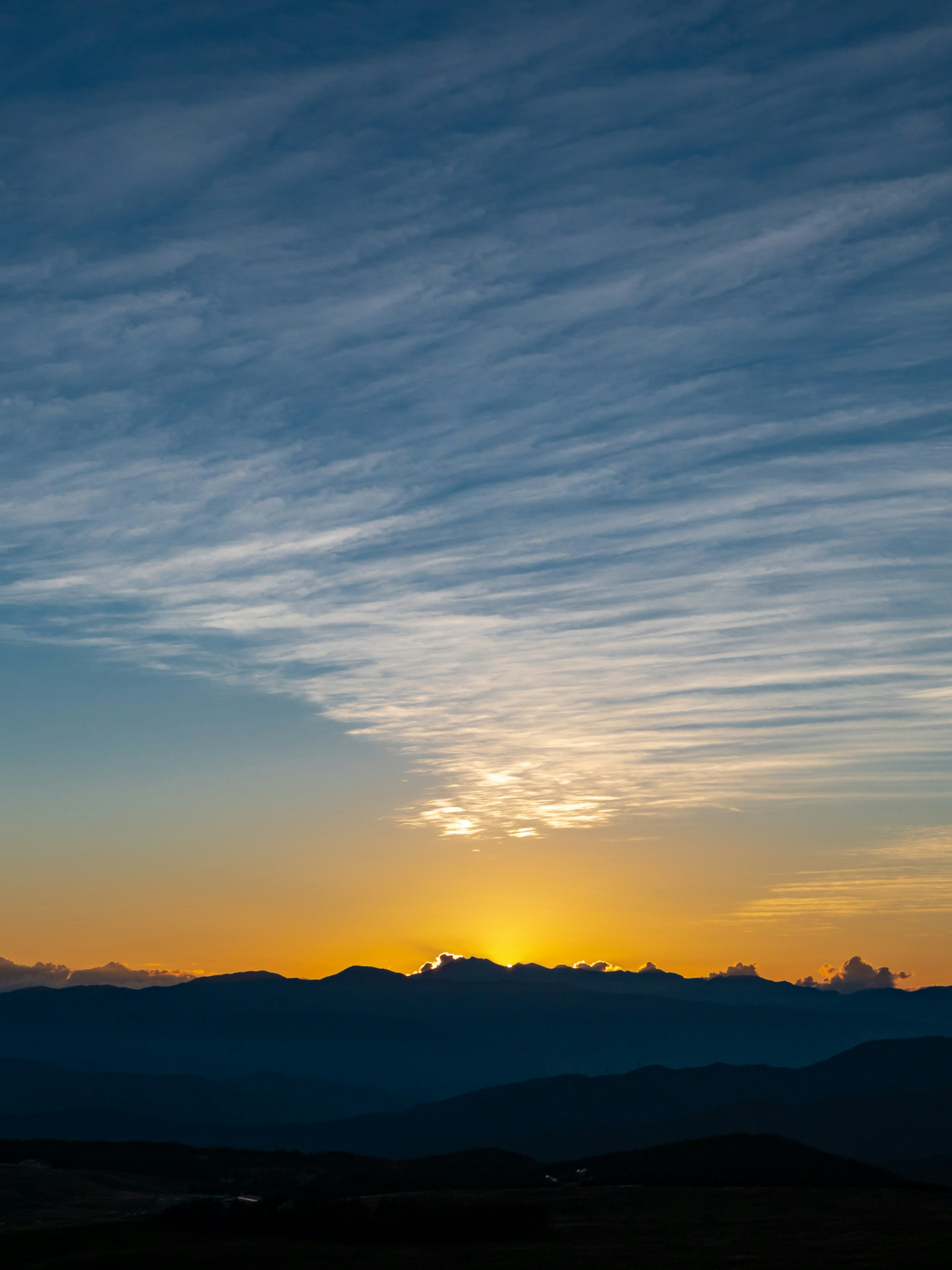 Un beau coucher de soleil derrière des montagnes avec un ciel rempli de nuages filandreux