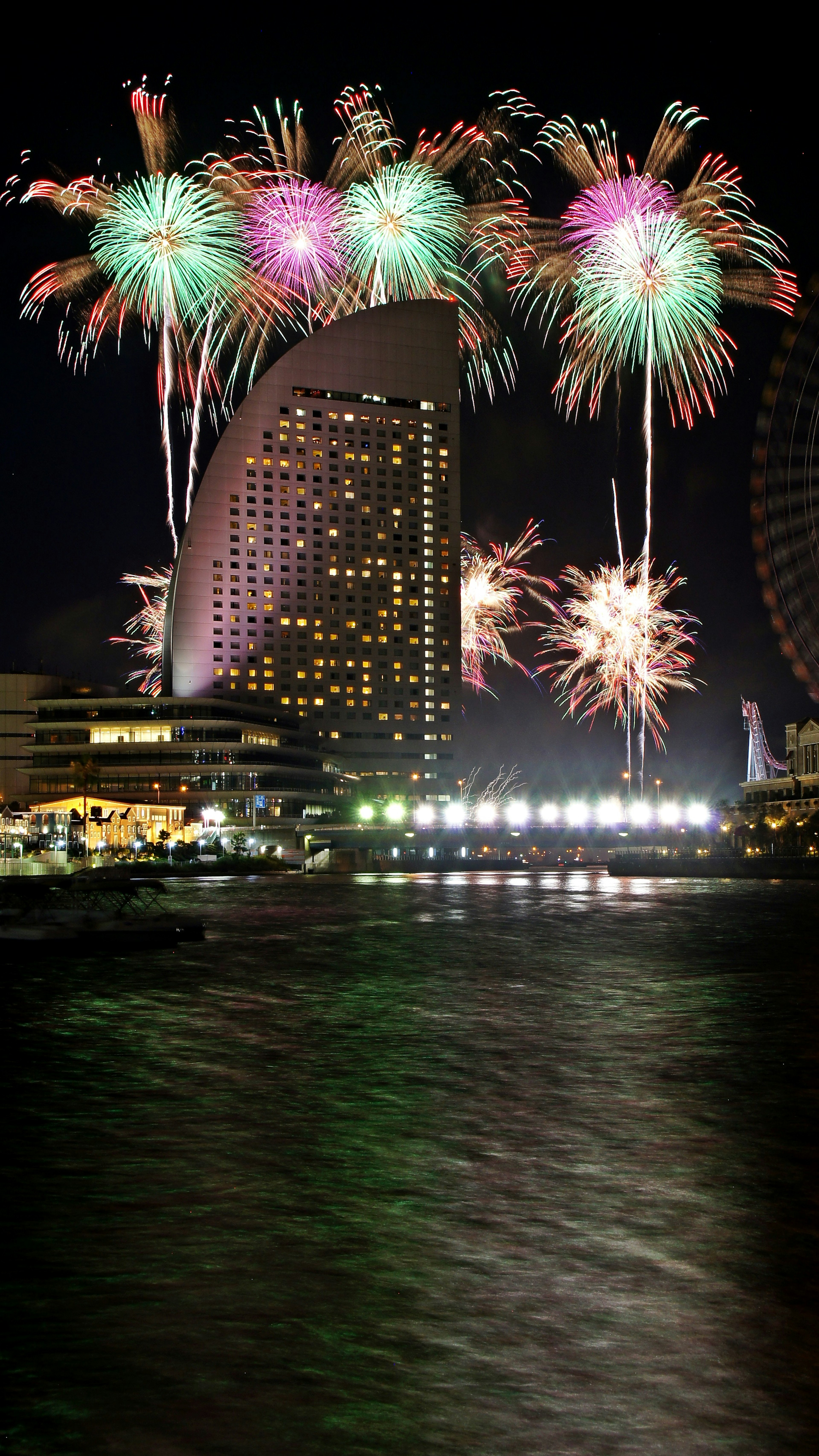 A stunning view of fireworks in the night sky and a high-rise building by the waterfront