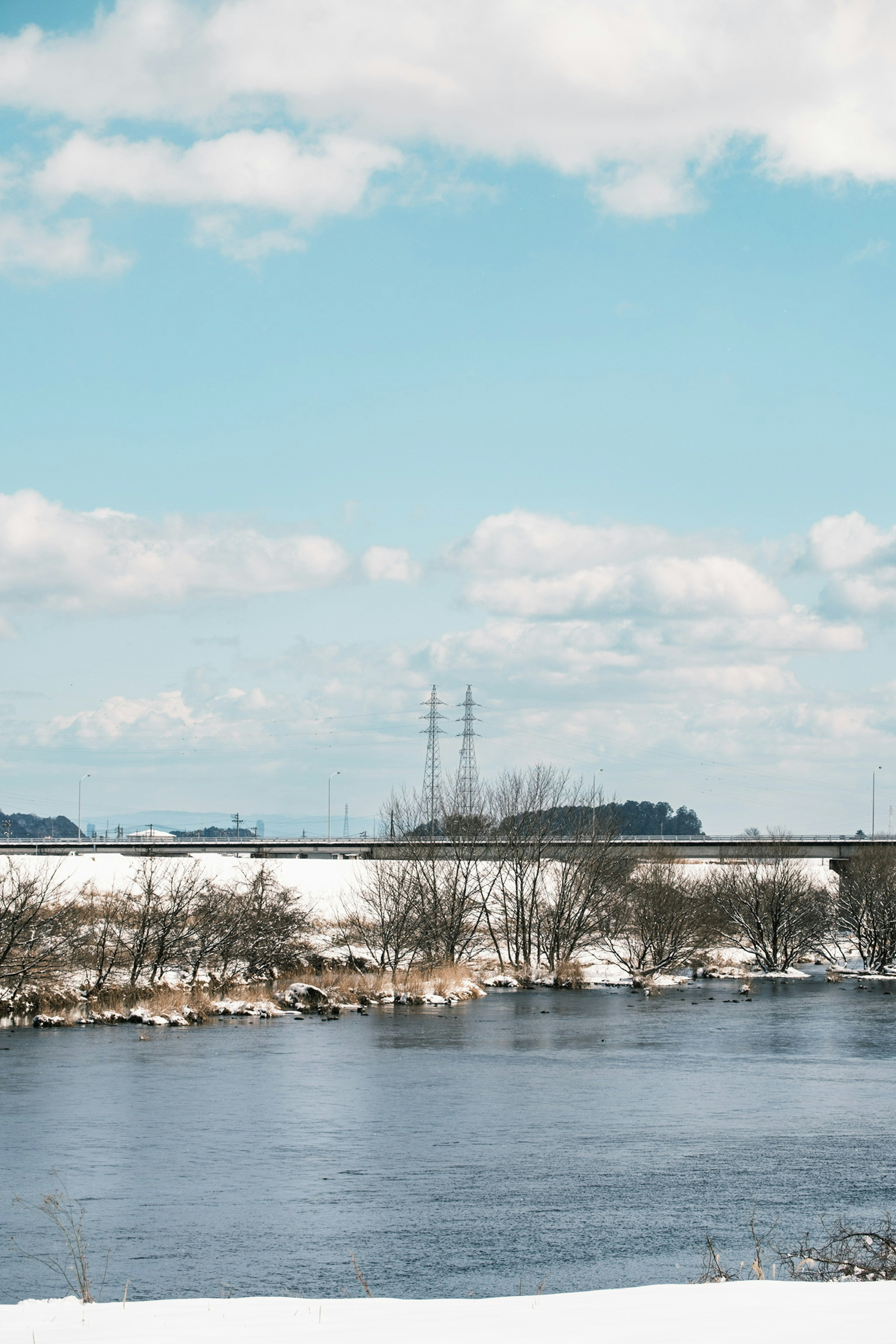 Winterlandschaft mit schneebedecktem Boden und Stromleitungen vor blauem Himmel