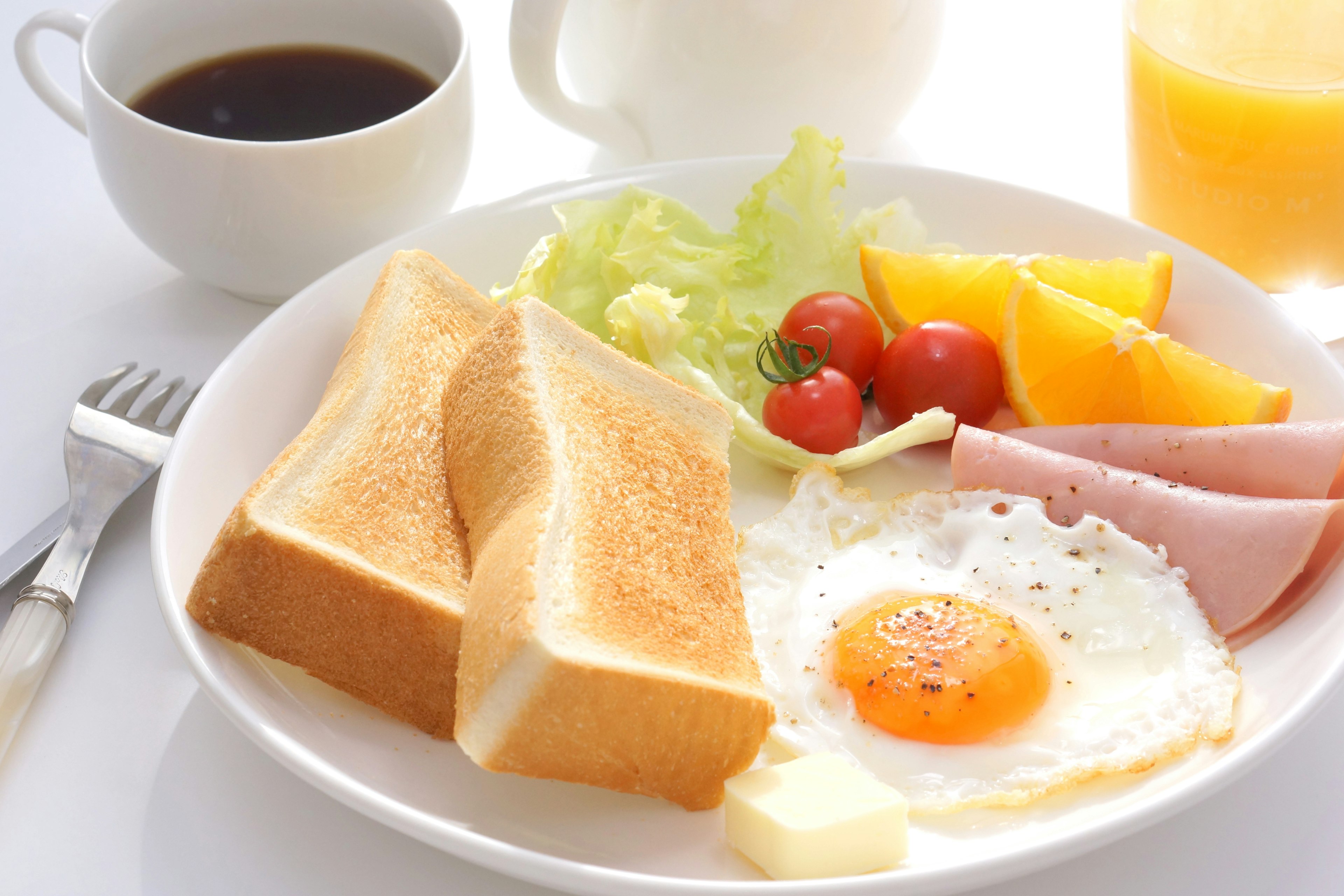 Piring sarapan dengan roti bakar, telur goreng, selada, tomat ceri, buah, dan ham