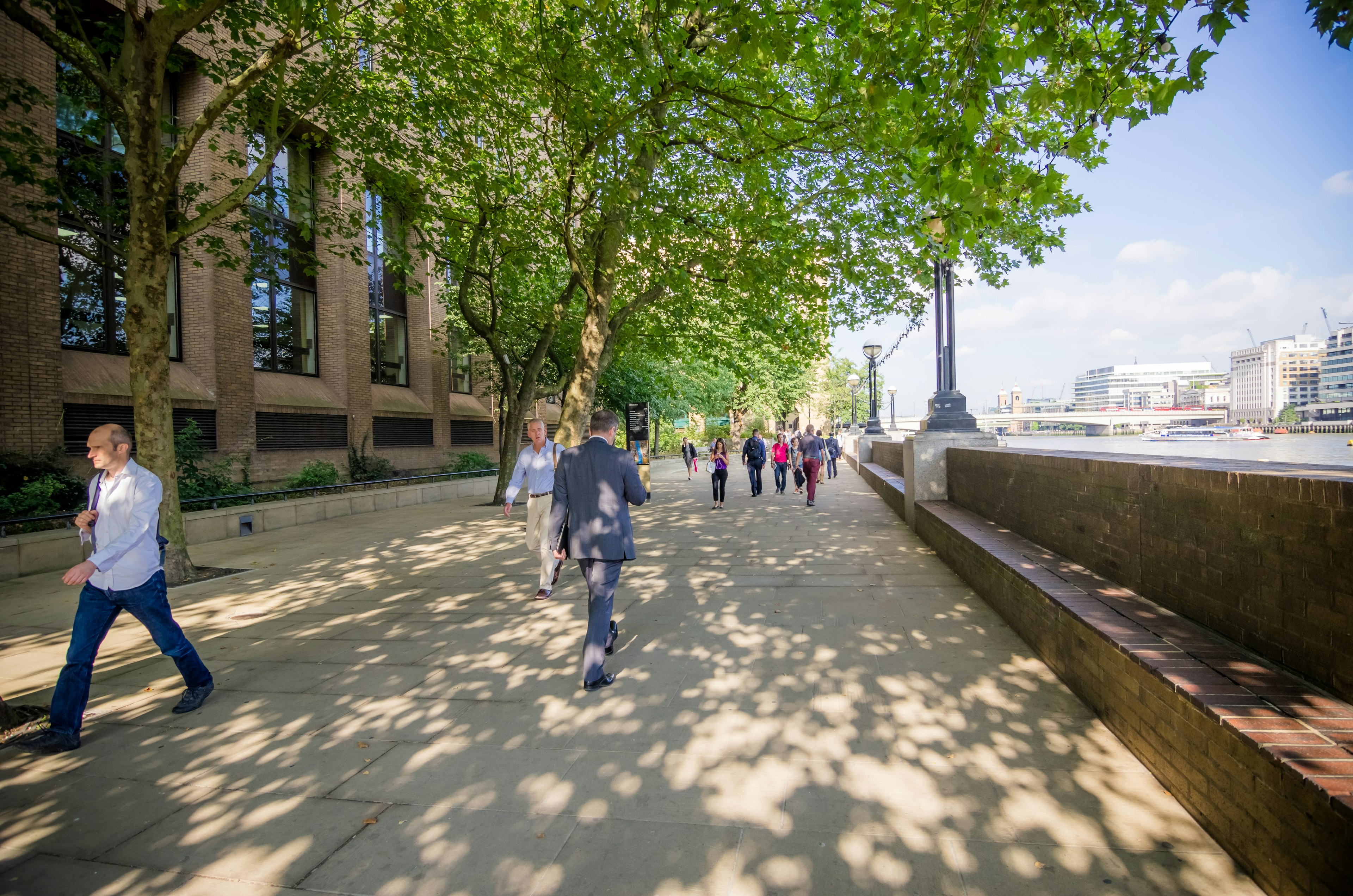 People walking along a tree-lined path by the river