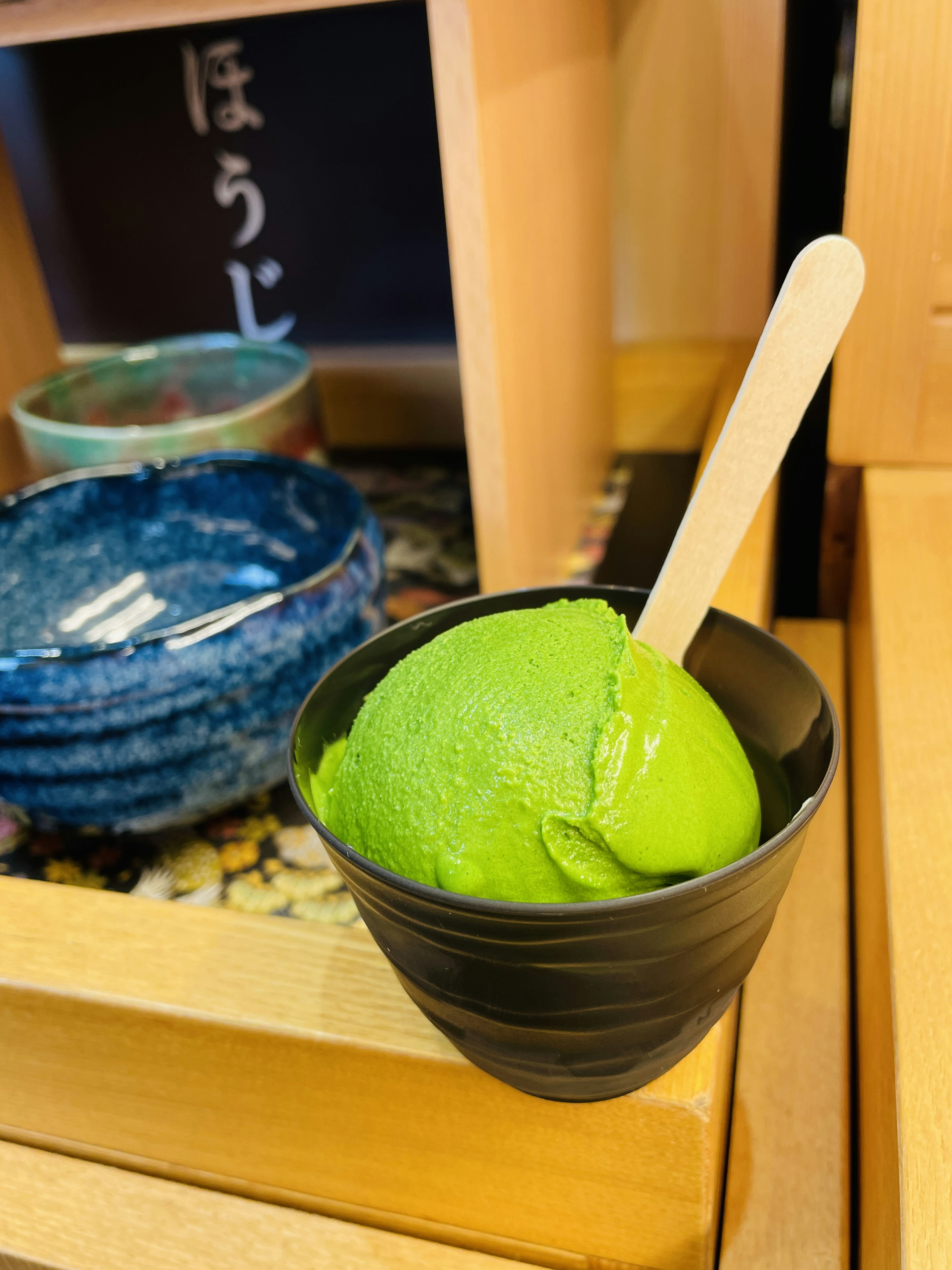 Green ice cream in a black cup with a wooden spoon