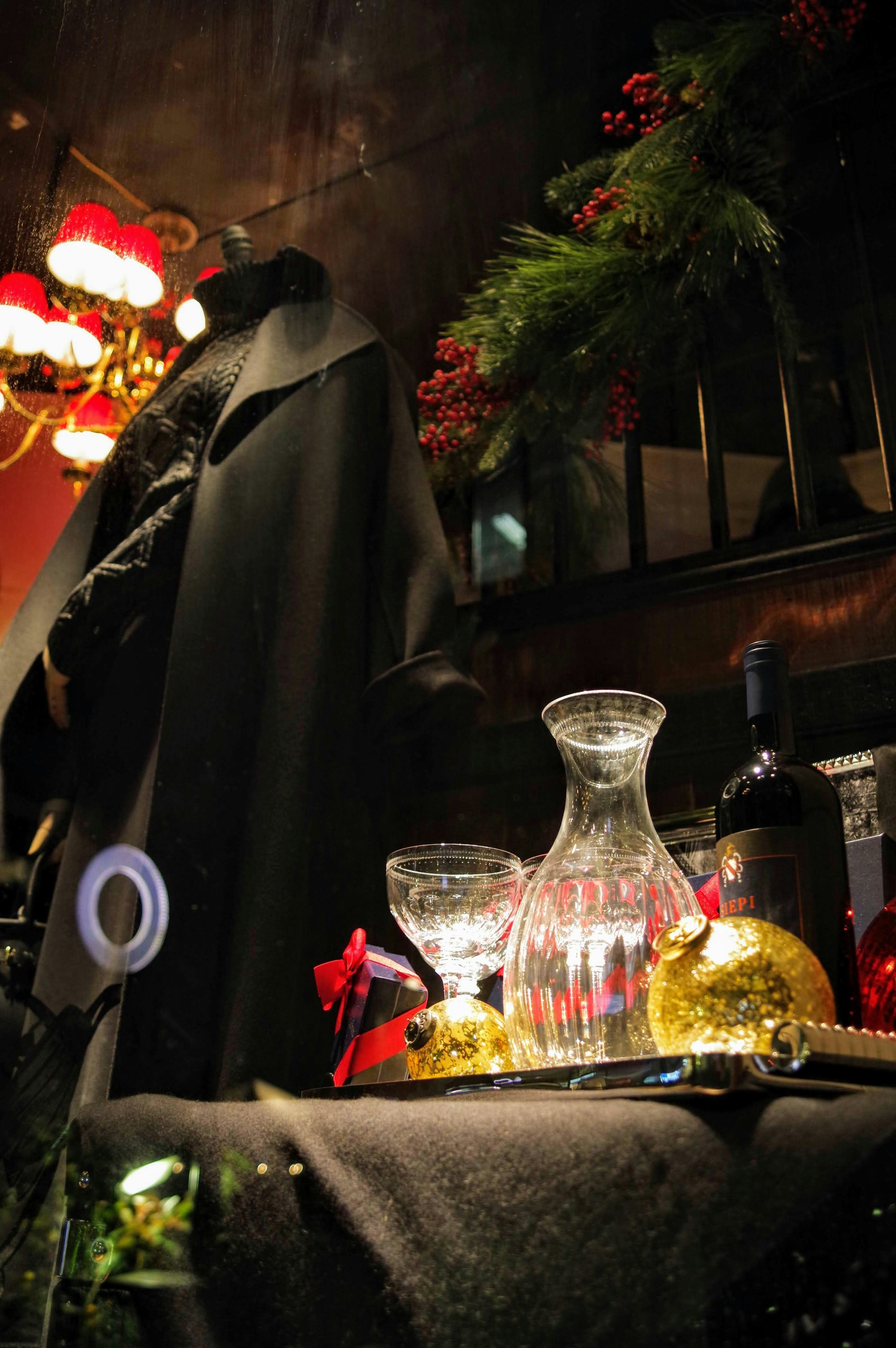 Una mesa decorada para Navidad con una jarra de vidrio y copas junto a una botella de vino en un entorno oscuro