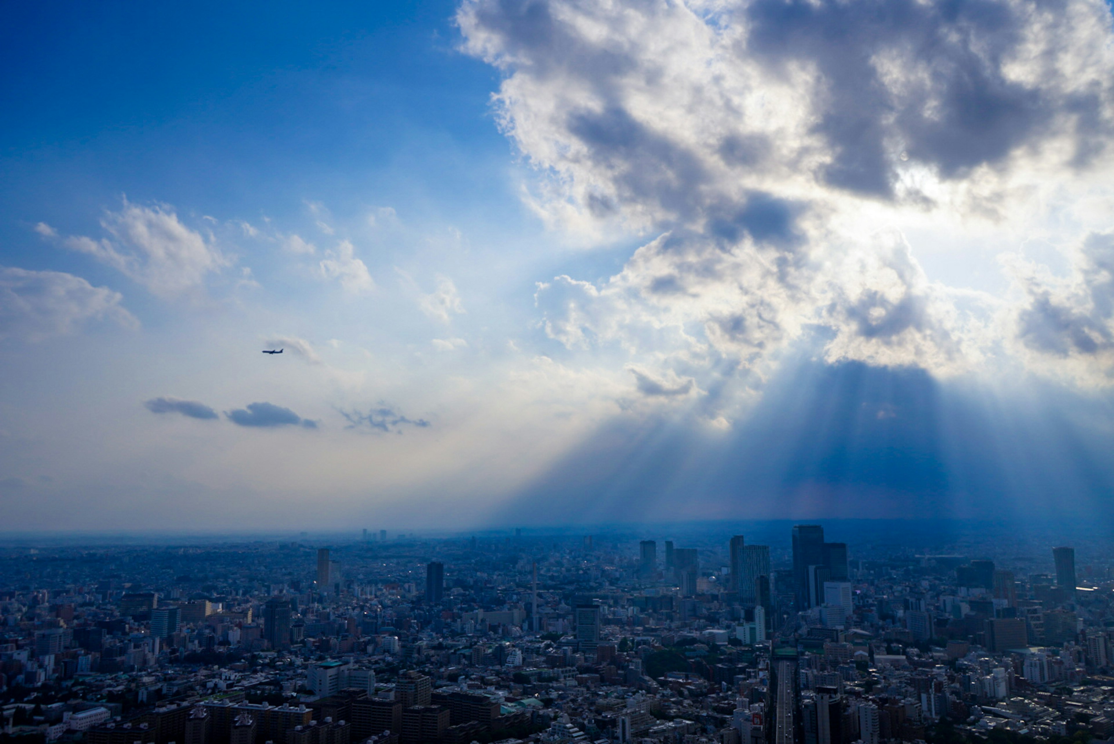 青い空と雲が広がる都市の風景に光が差し込む