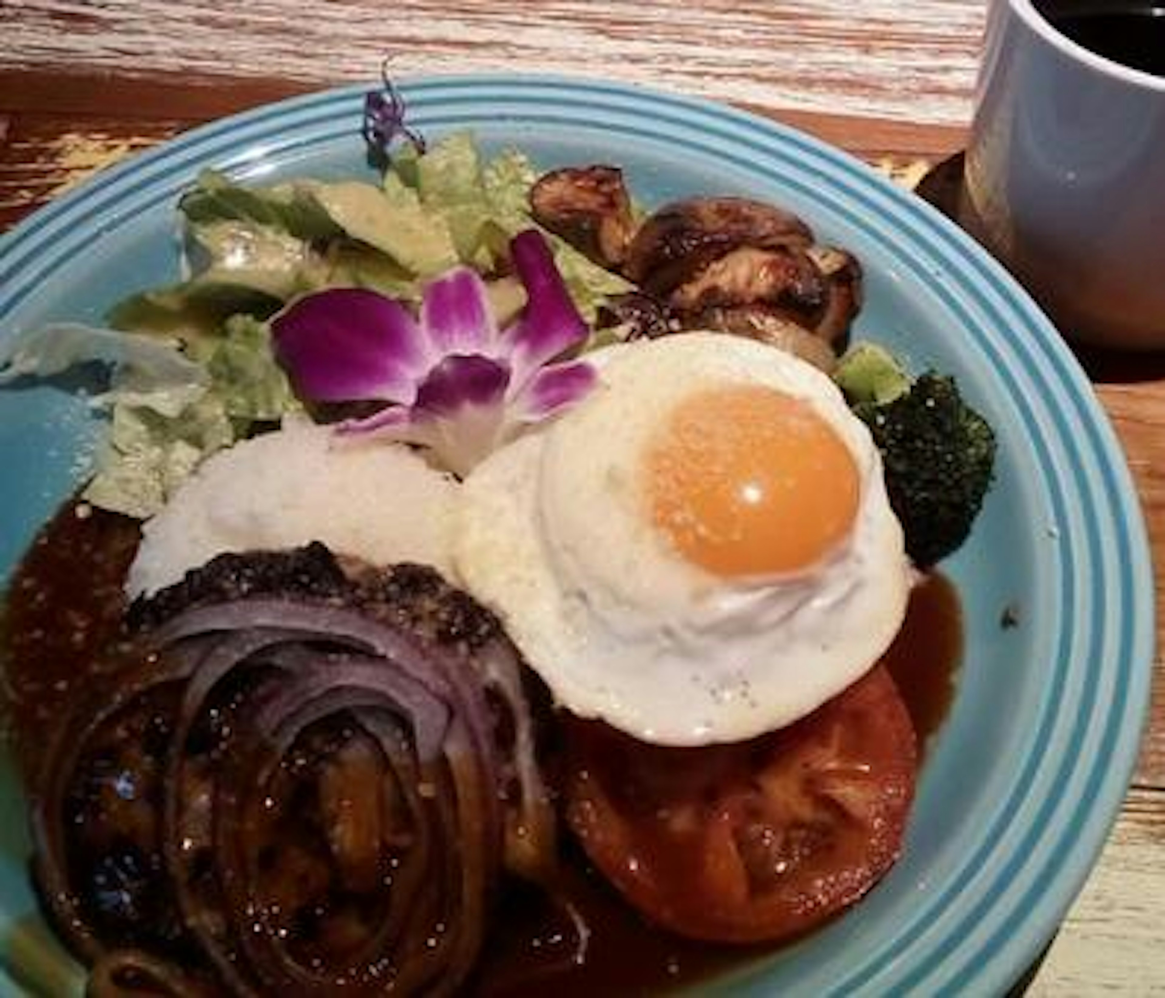 Piring dengan nasi dan telur mata sapi disertai sayuran berwarna-warni dan hiasan bunga