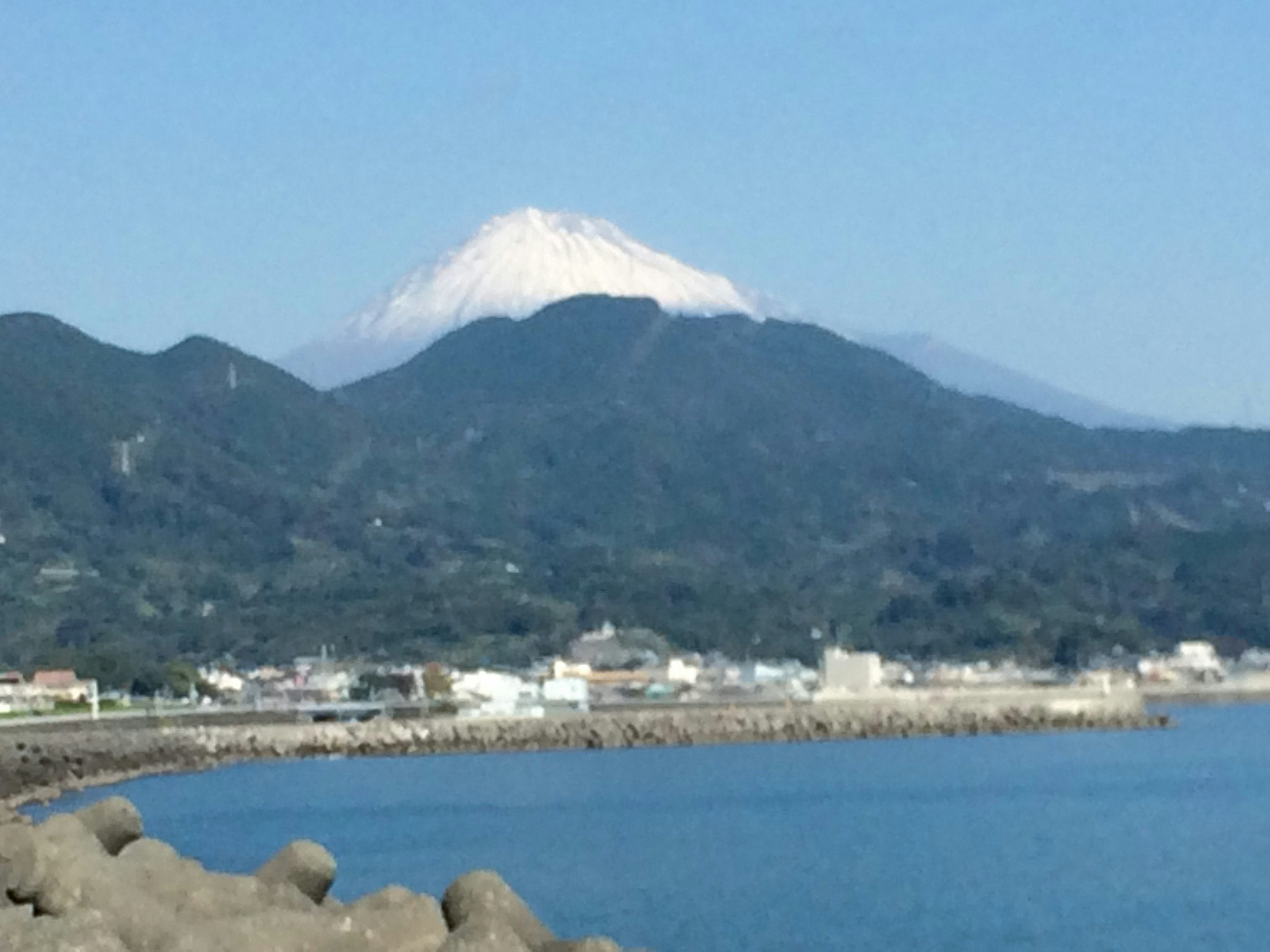 Scenic view featuring Mount Fuji capped with snow against a blue sea and hills