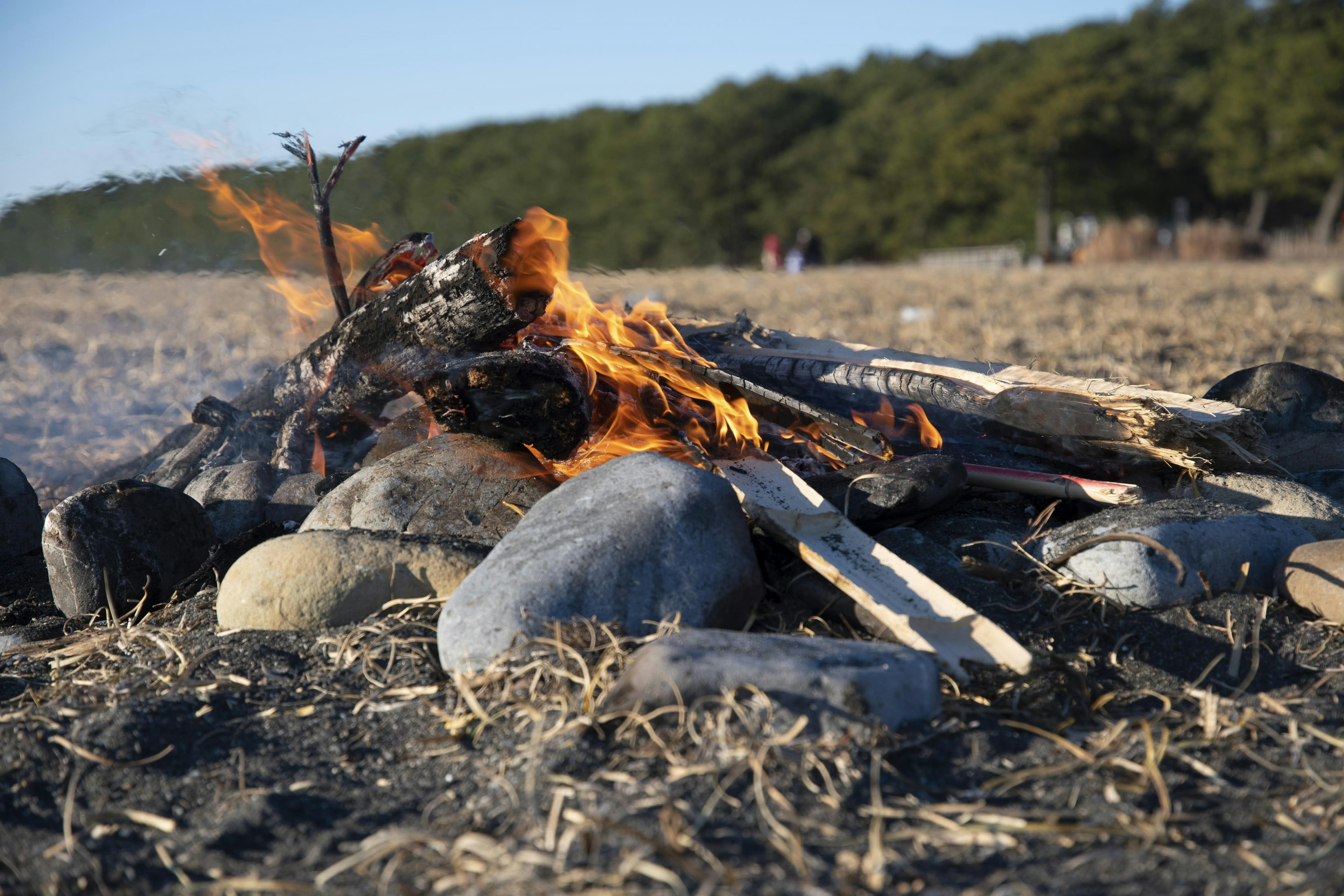 Campfire burning on the beach surrounded by stones