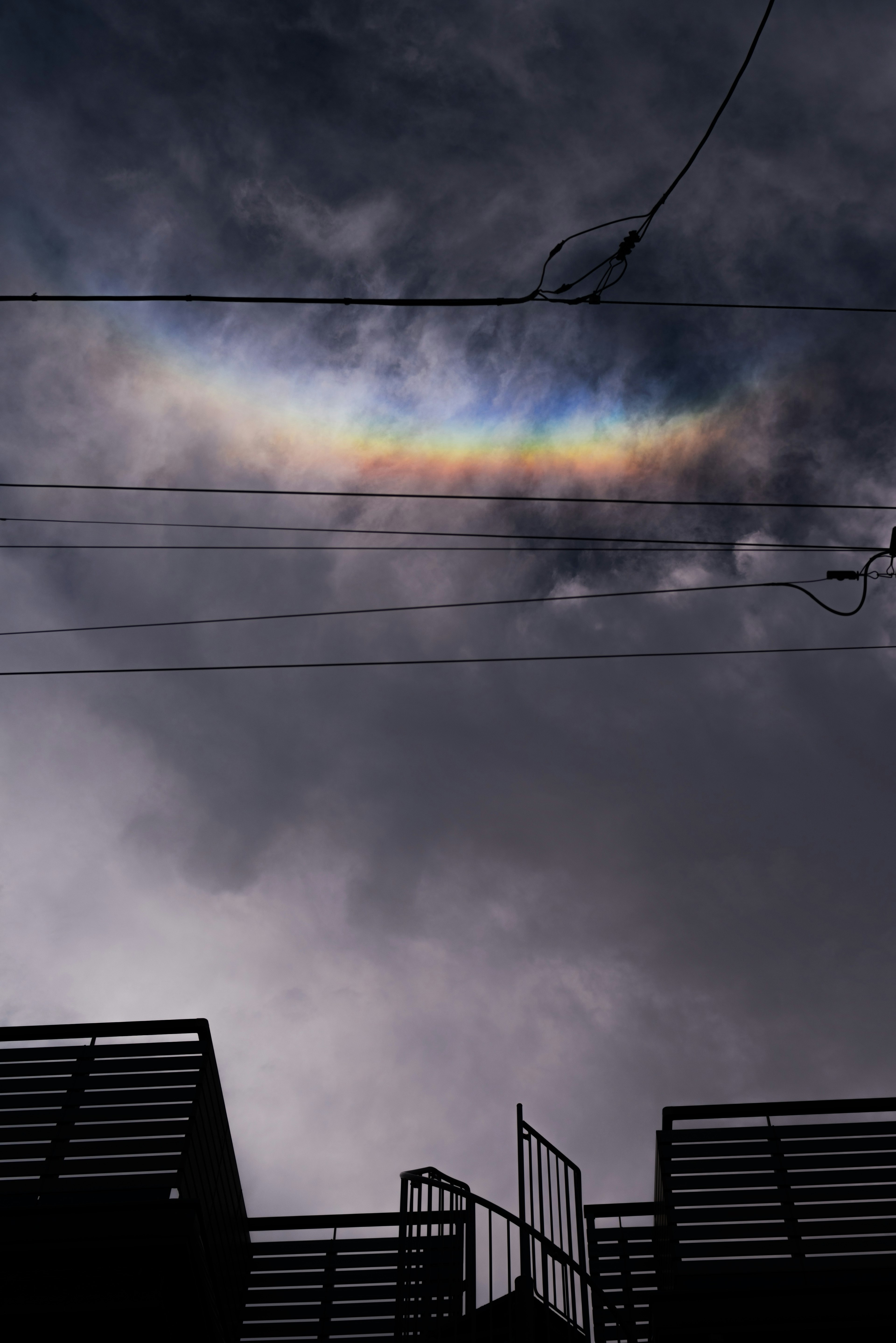 暗い雲に浮かぶ虹色の弧と電線の風景