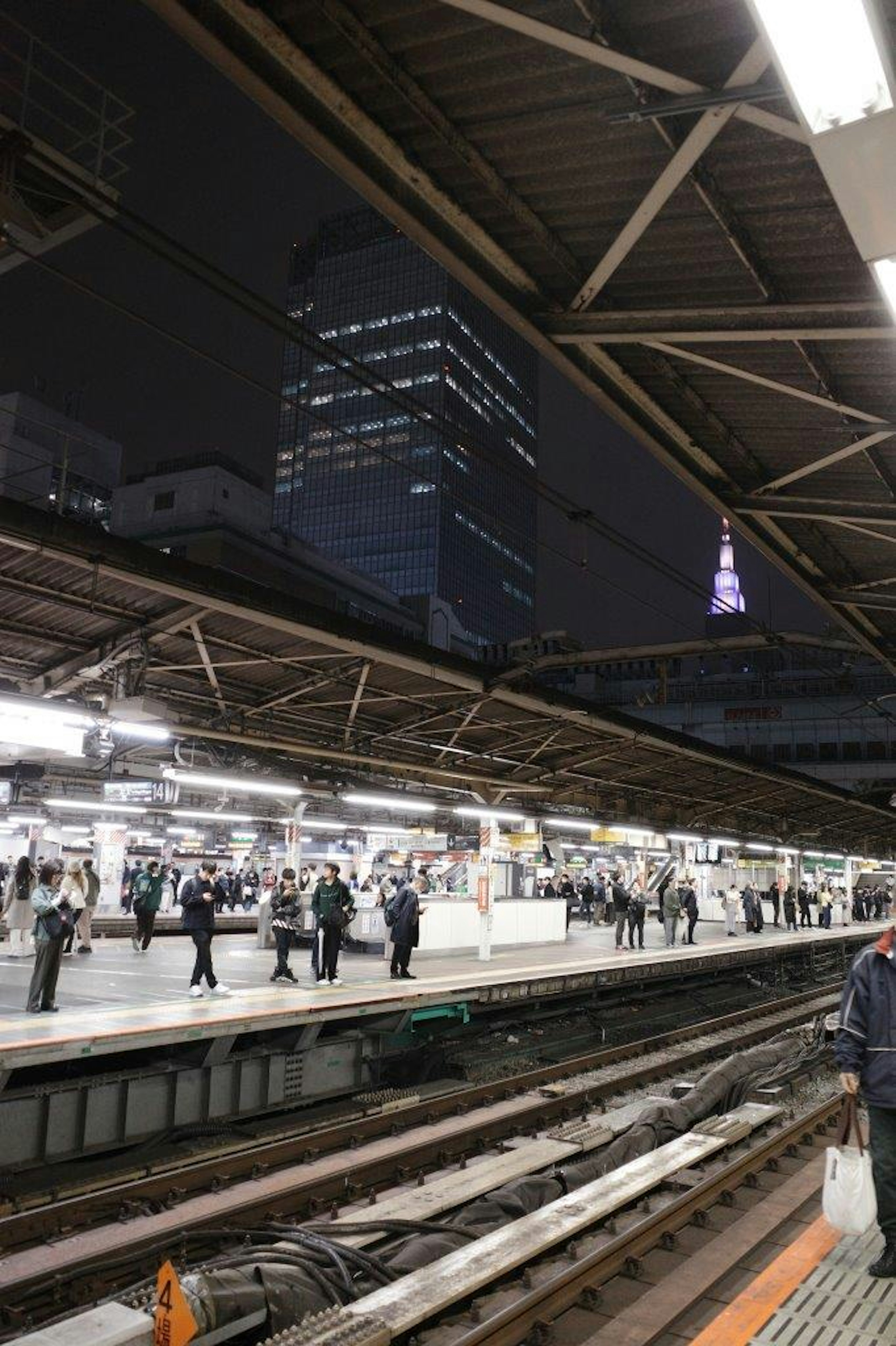 夜の駅で多くの人々が待機している様子と遠くに見える東京タワー