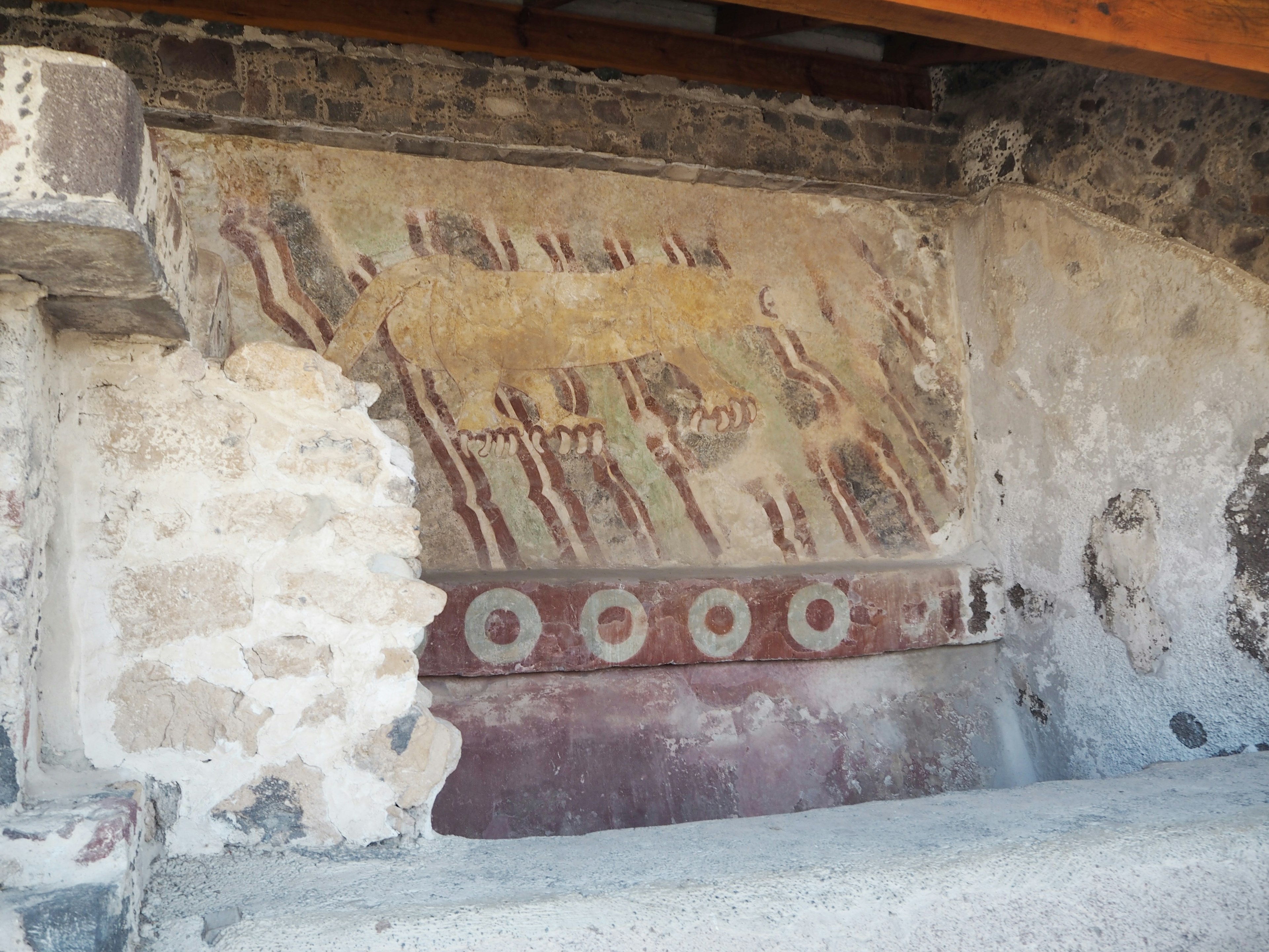 Sección de una pared antigua con mural pintado que presenta tonos terrosos y patrones geométricos