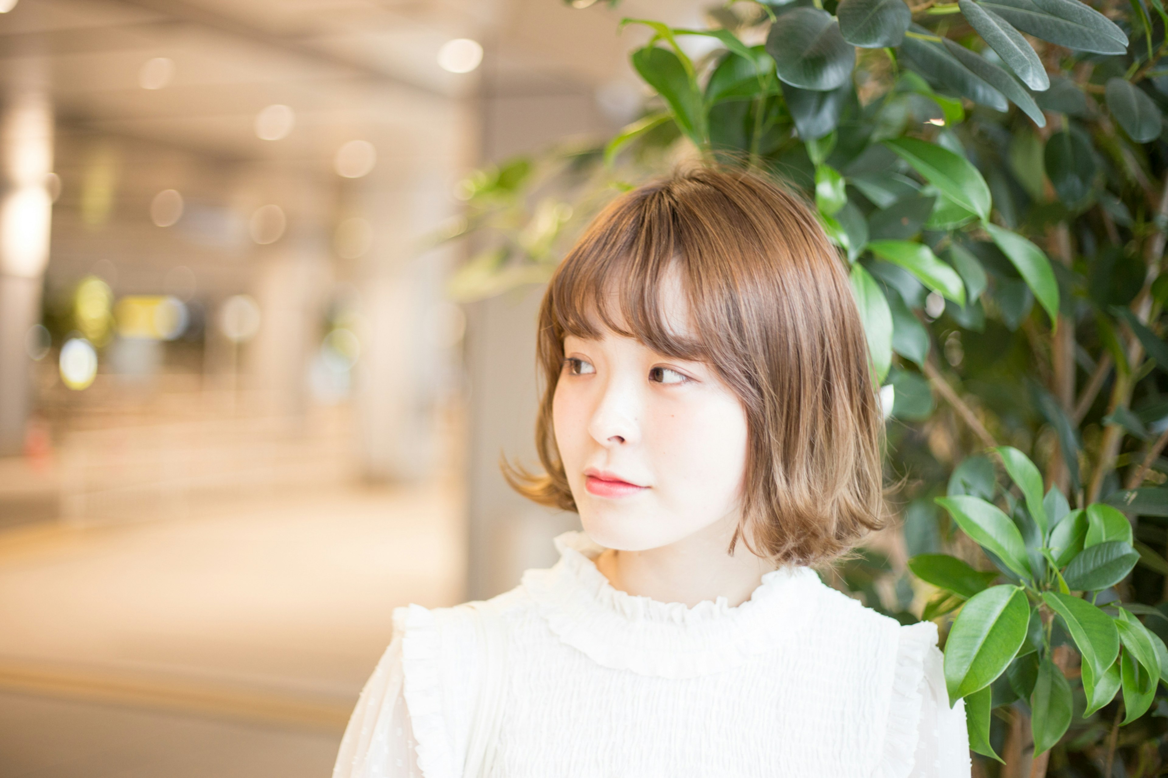 Una joven con una blusa blanca de pie junto a una planta verde