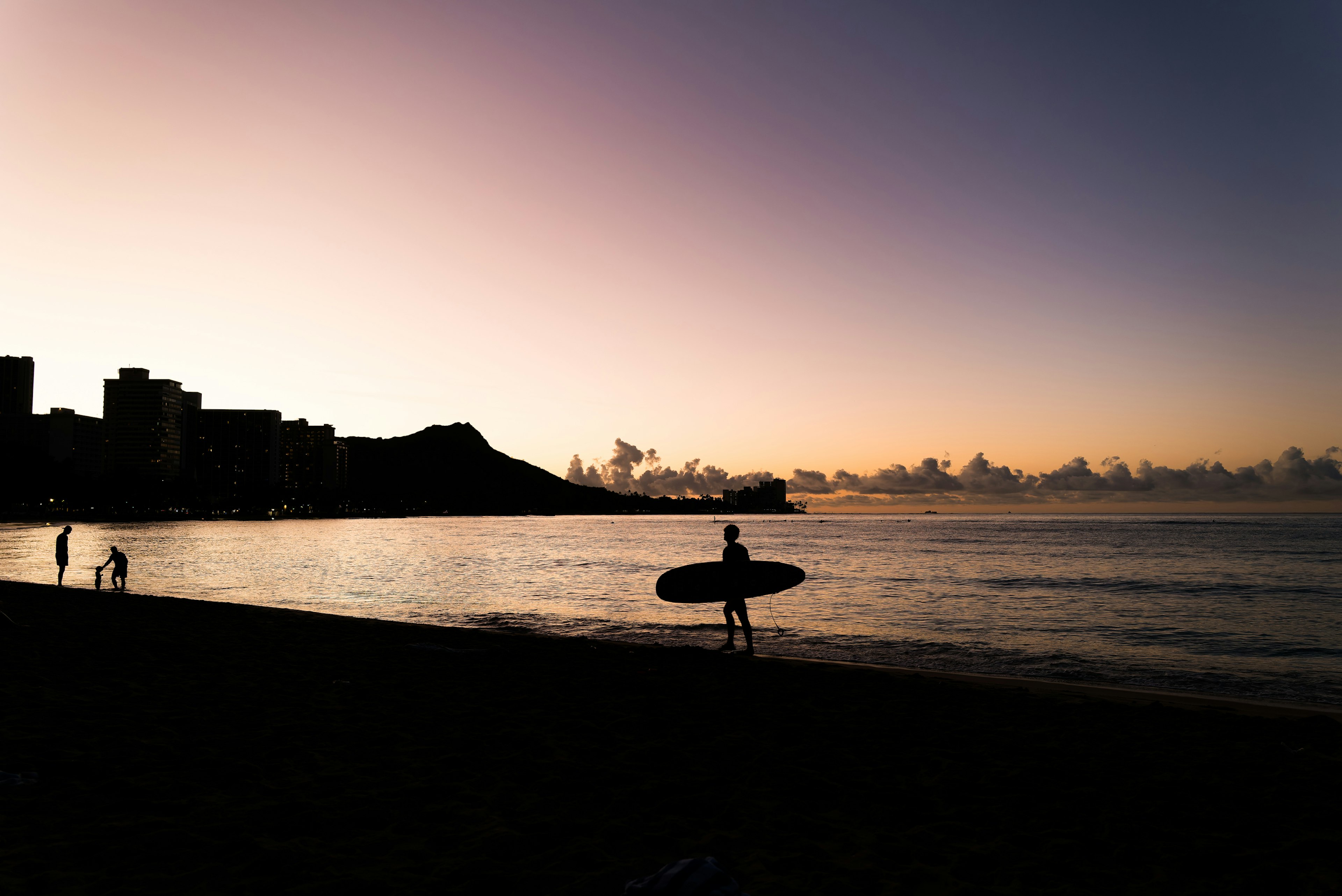 Silhouette of a surfer against a sunset with calm waters