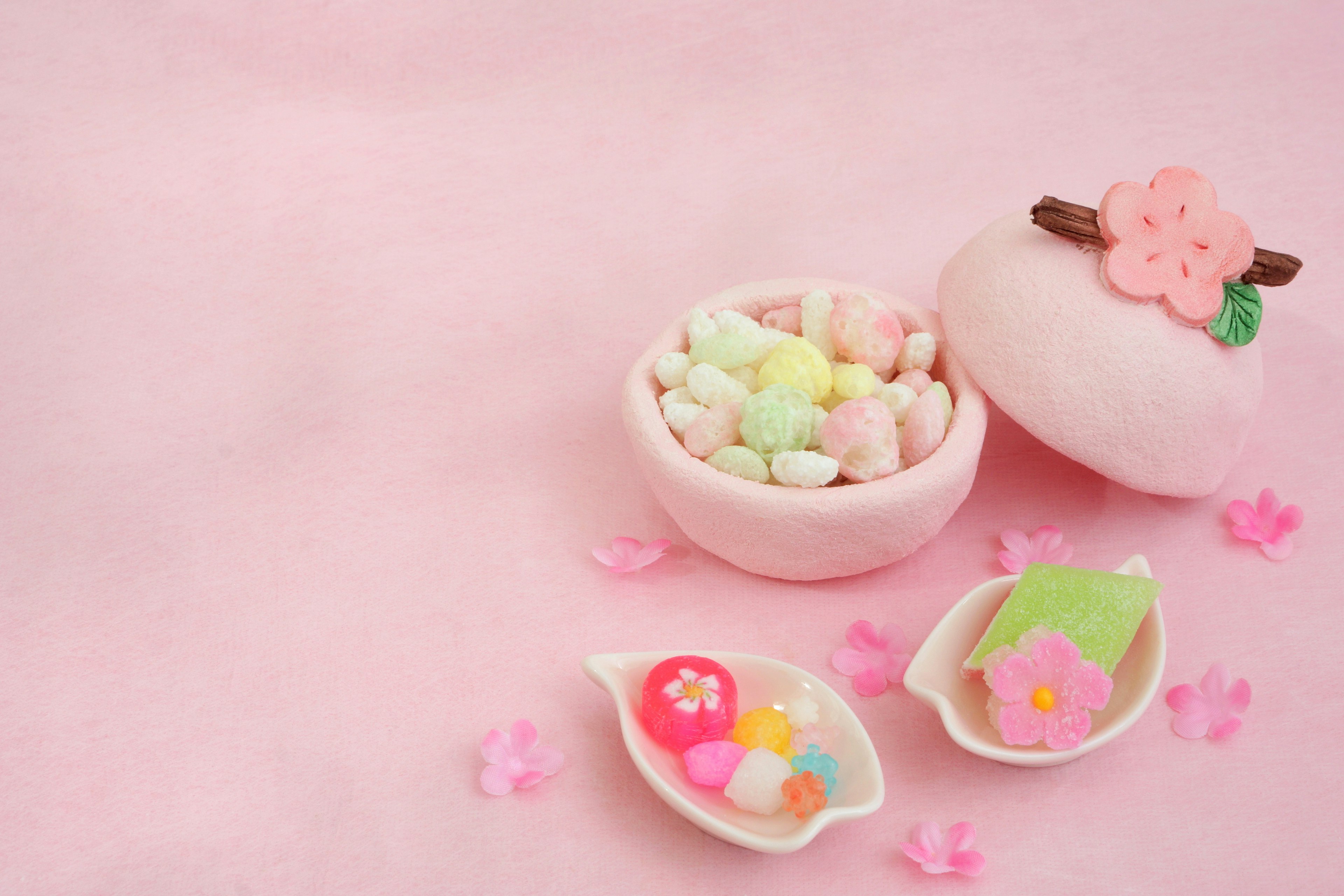 Colorful candies in a pink bowl decorated with cherry blossoms on a pink background