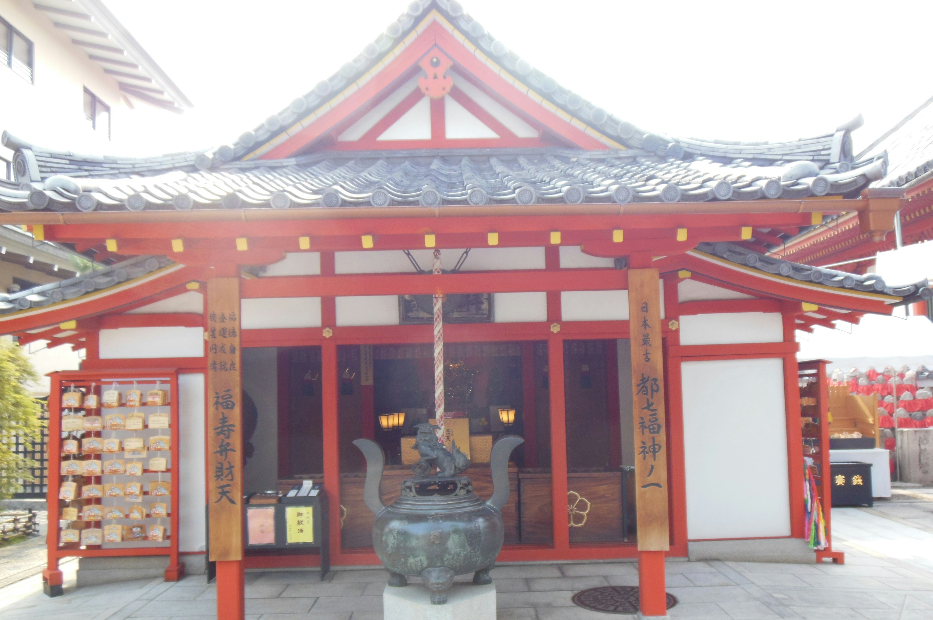 Exterior view of a Japanese shrine with red roof and pillars featuring a smoke-emitting incense burner in front