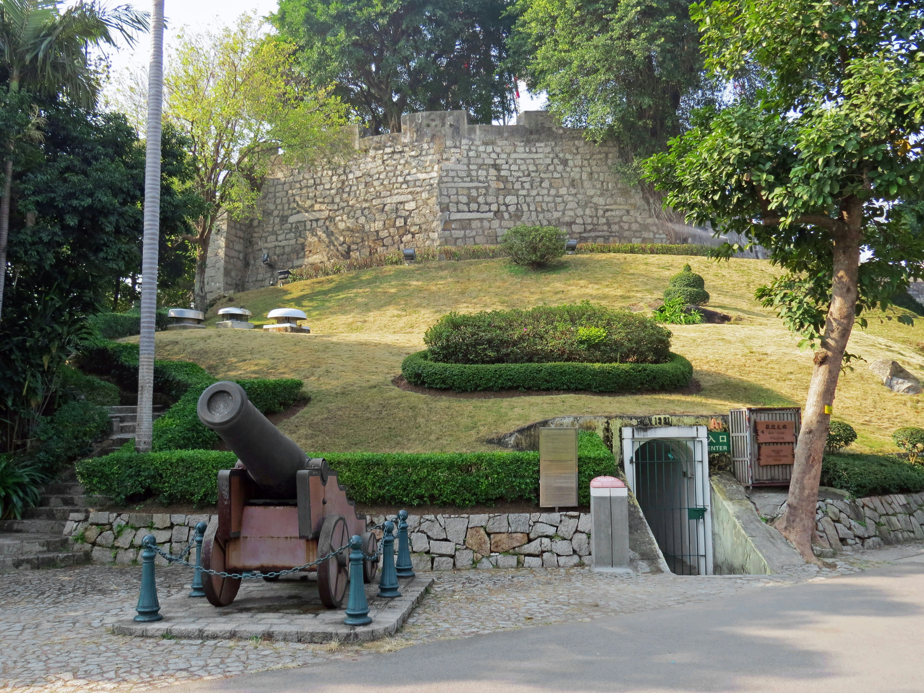 A historic cannon in front of a stone fortress surrounded by green landscaping