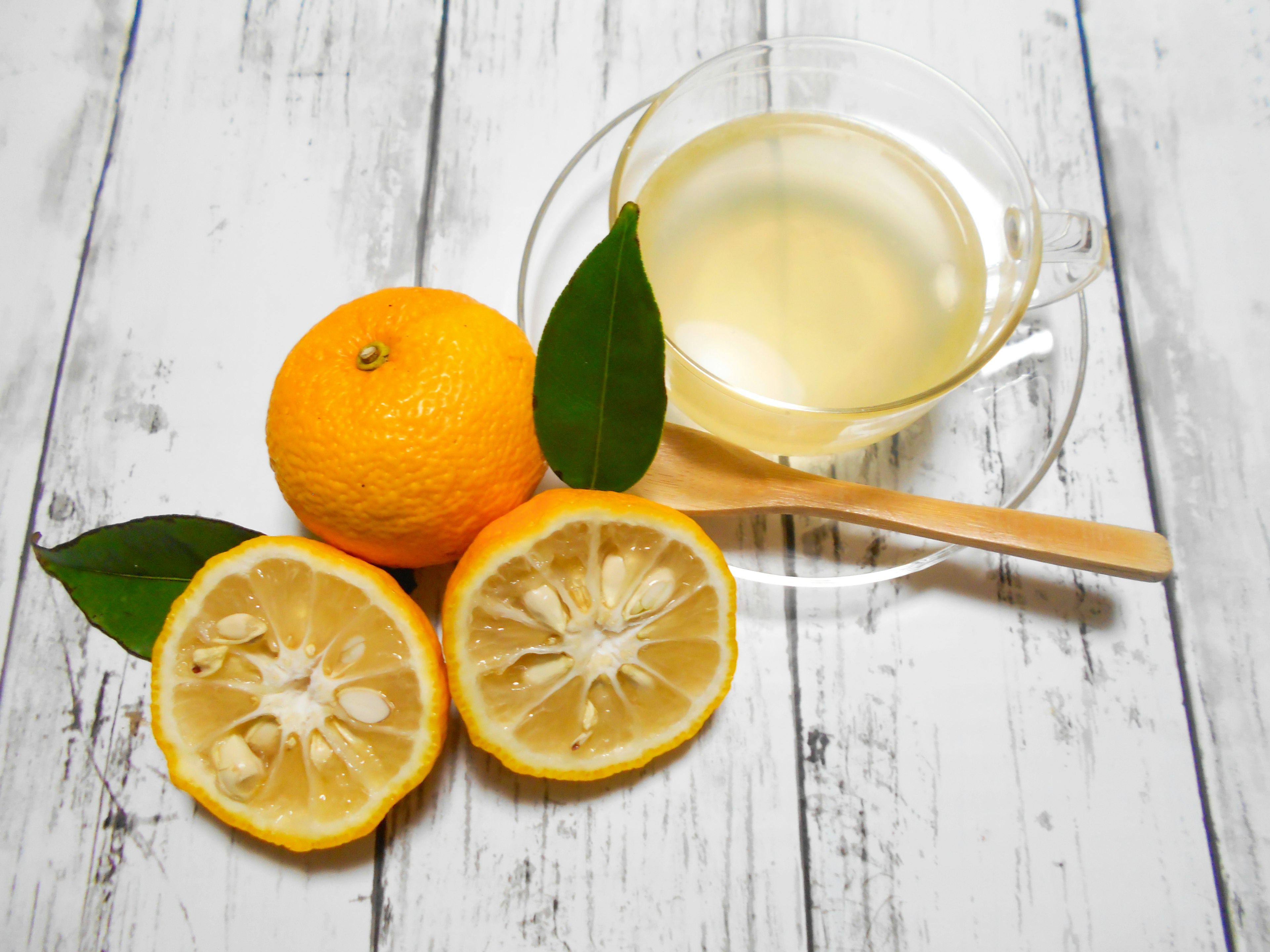 An arrangement of an orange and lemon slices next to a transparent drink in a glass cup