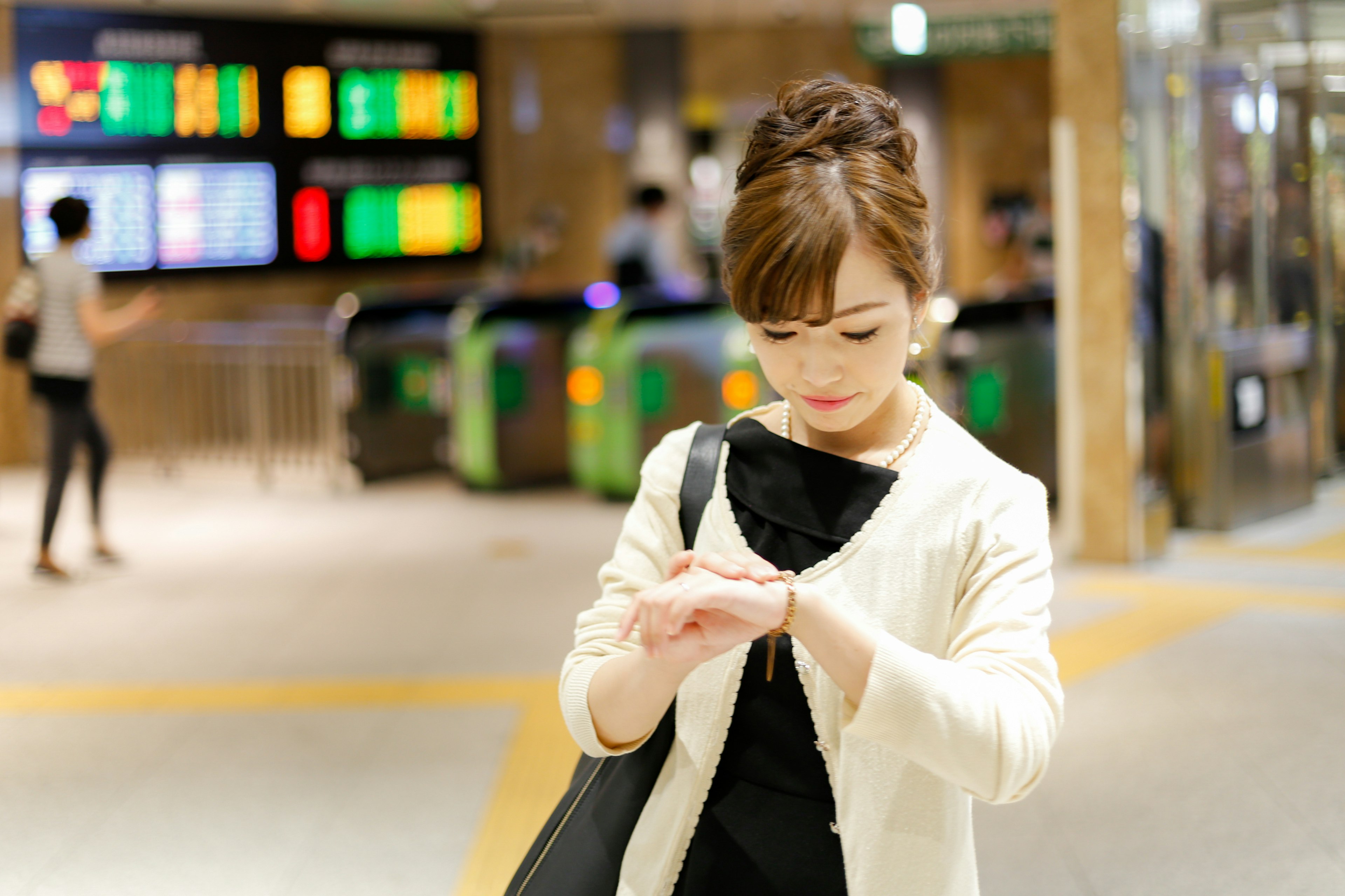 Une femme vérifiant sa montre dans une gare avec des panneaux d'affichage colorés en arrière-plan