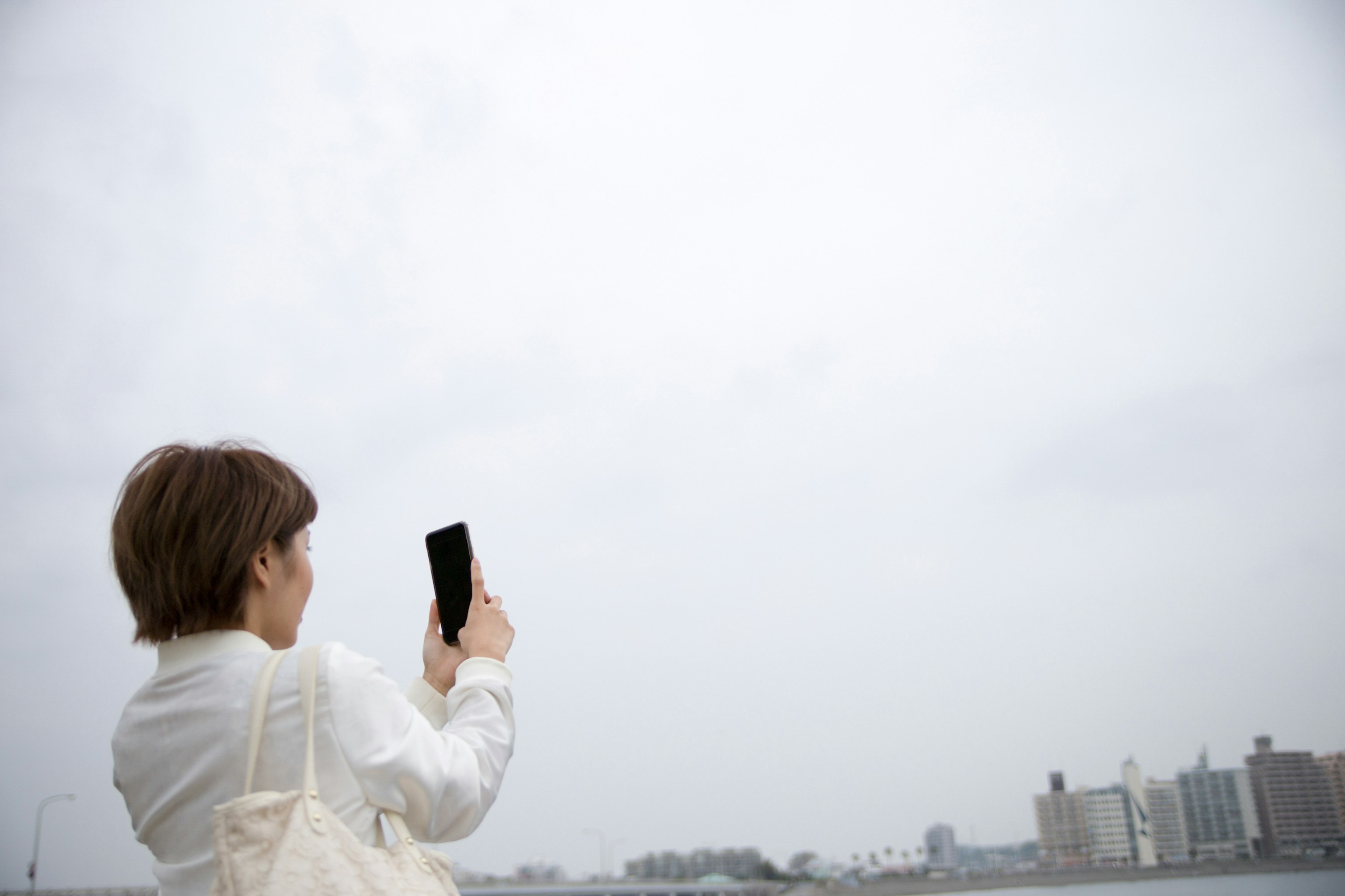 Une femme prenant une photo avec son smartphone sous un ciel nuageux