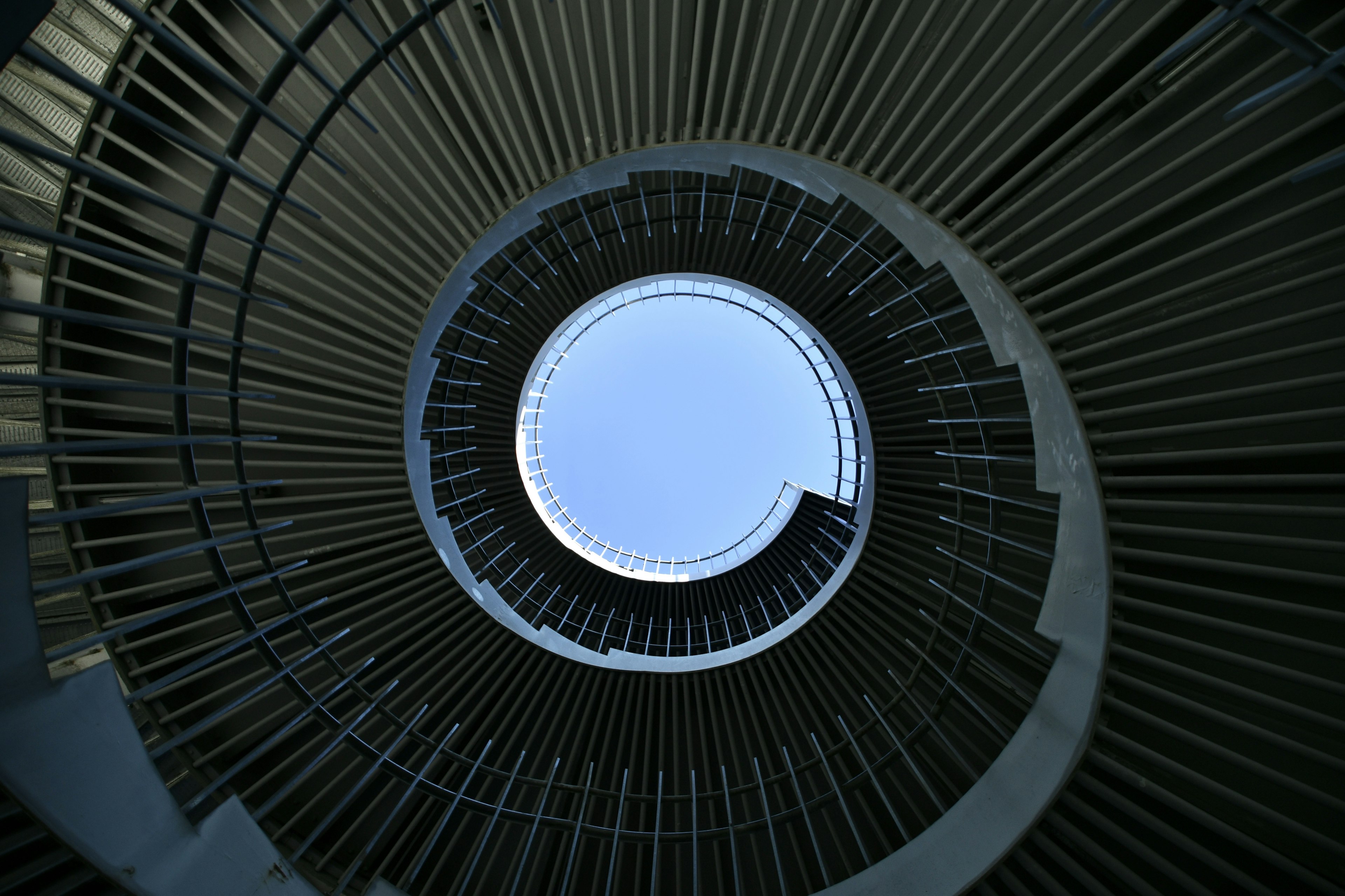 View from the bottom of a circular spiral staircase with visible blue sky