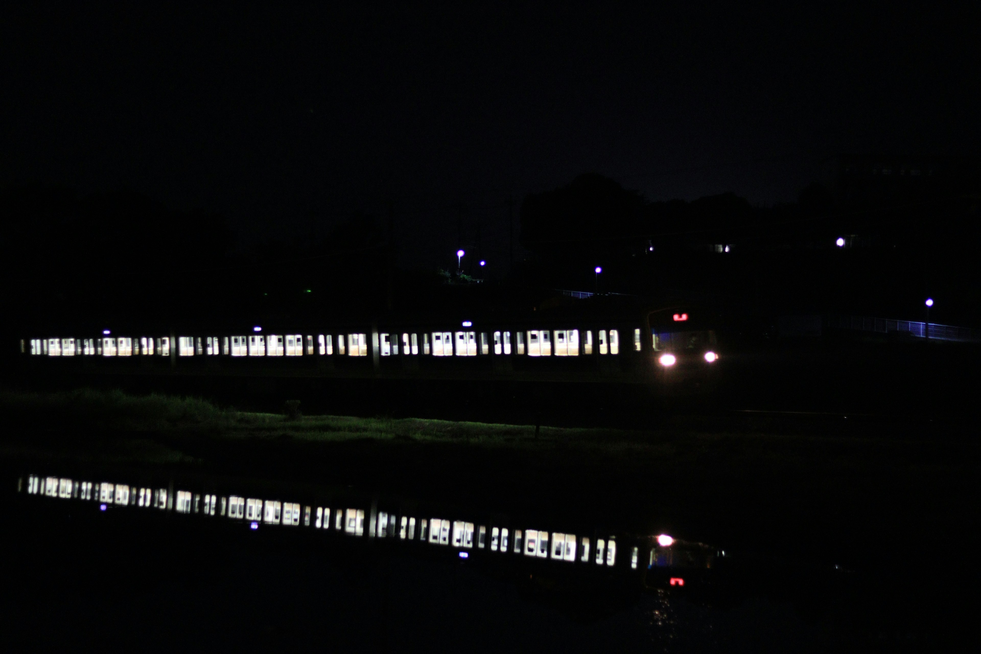 Cahaya kereta yang memantul di sungai di malam hari dengan lampu jalan di sekitarnya