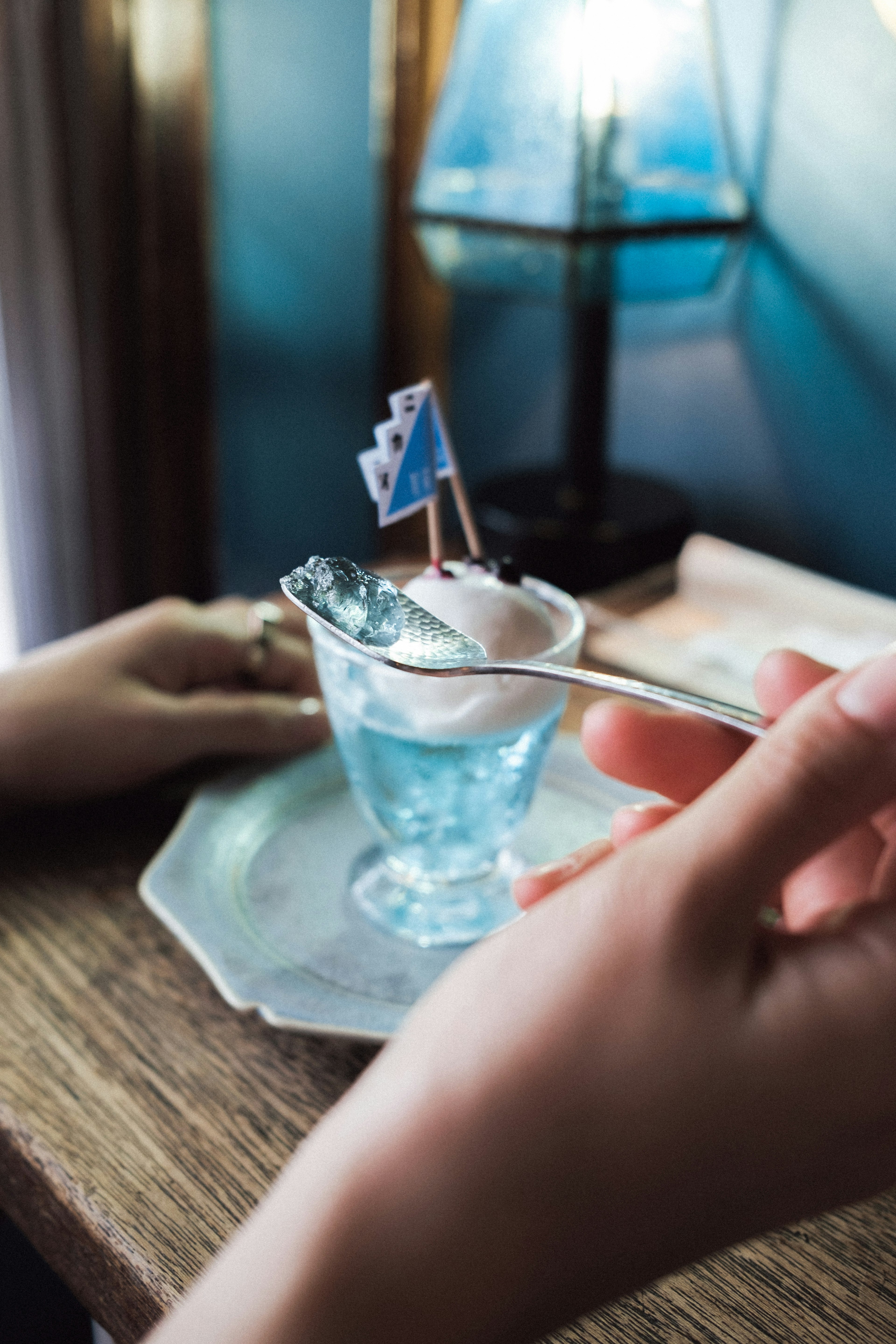 Sebuah tangan memegang sendok di atas gelas dengan minuman biru dan bendera kecil