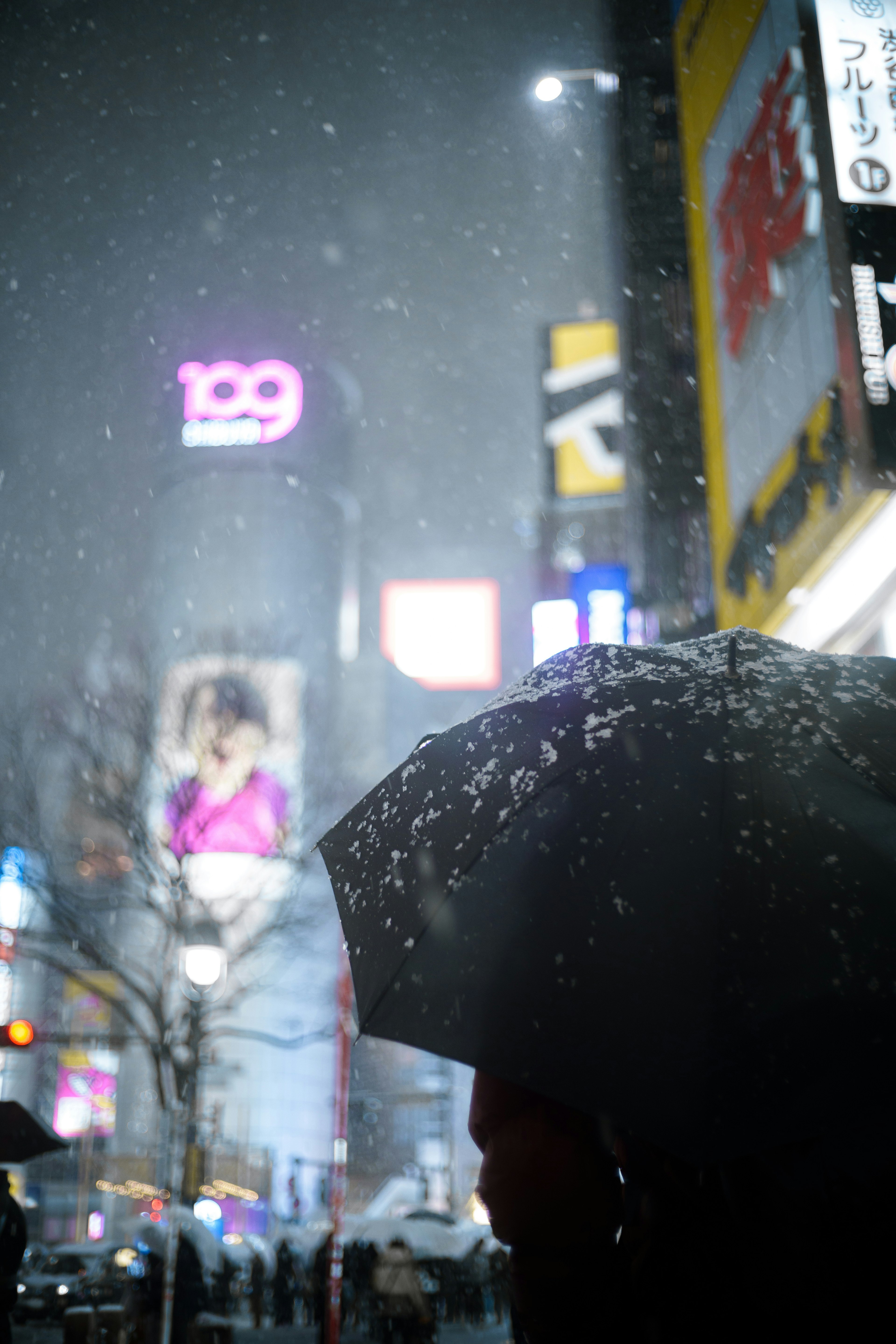 Silhouette of a person holding an umbrella in falling snow with bright billboards