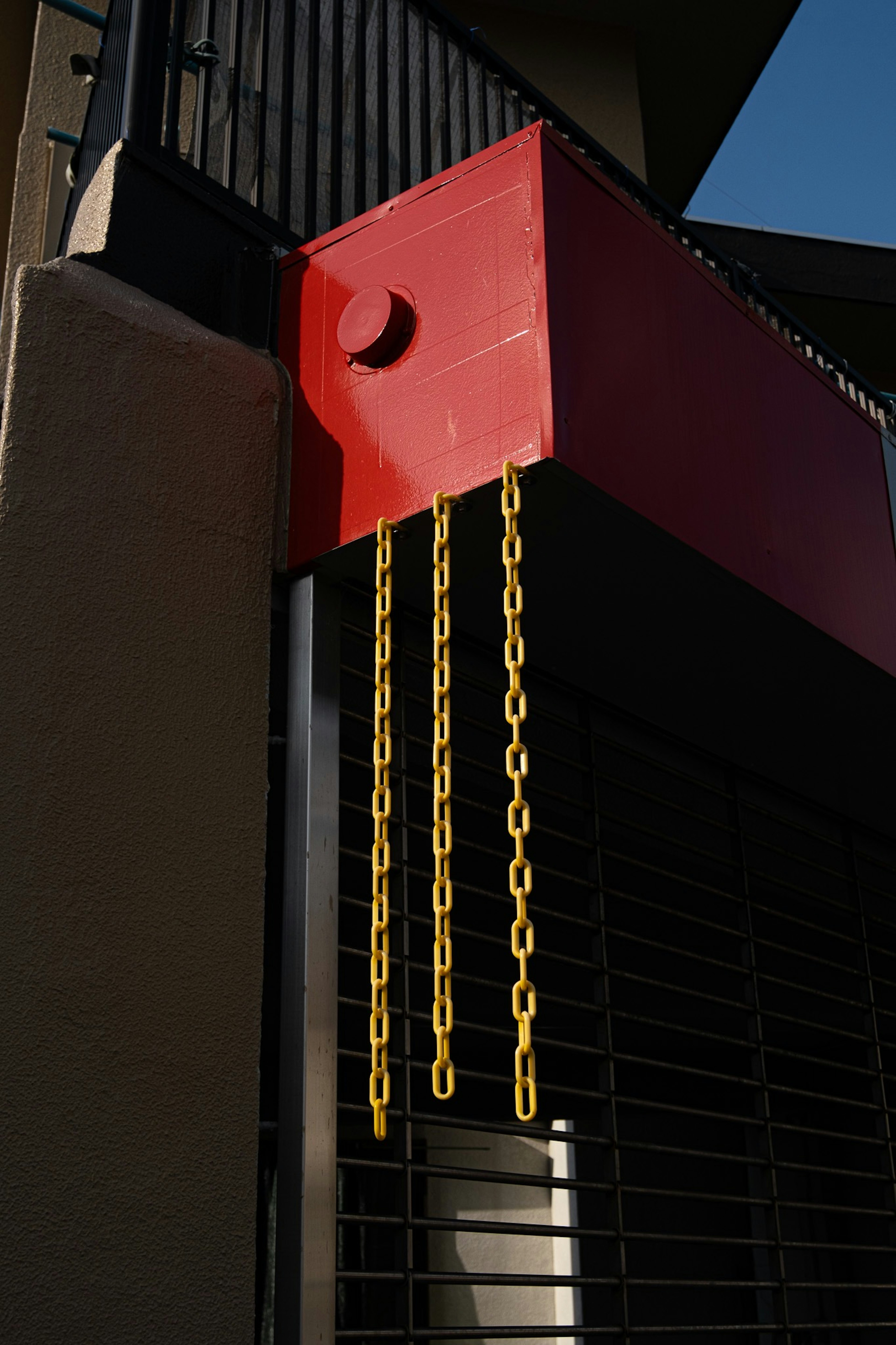 Cadenas amarillas colgando de una estructura roja contra una persiana negra