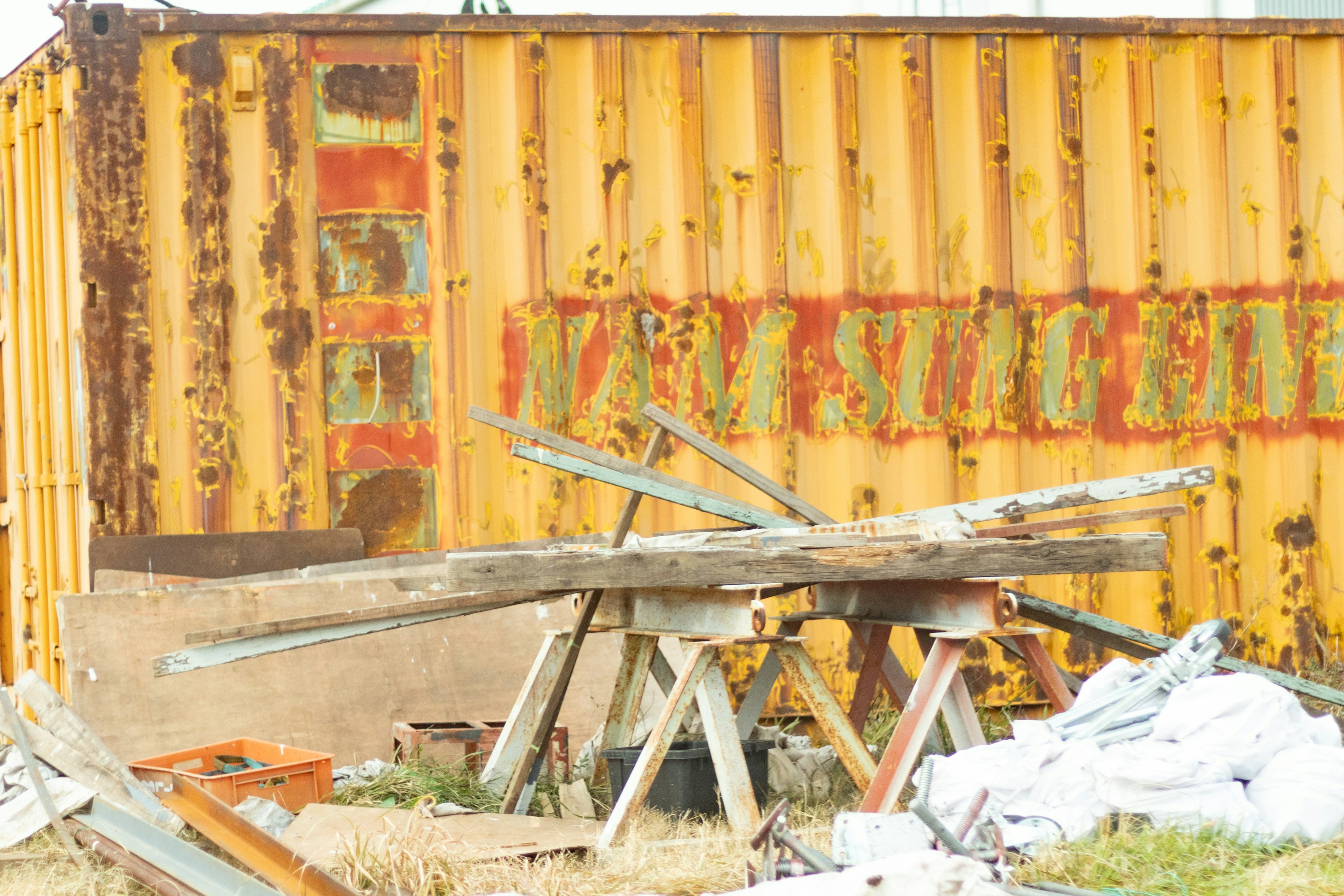 A weathered yellow shipping container with rusty patches surrounded by scrap wood and debris