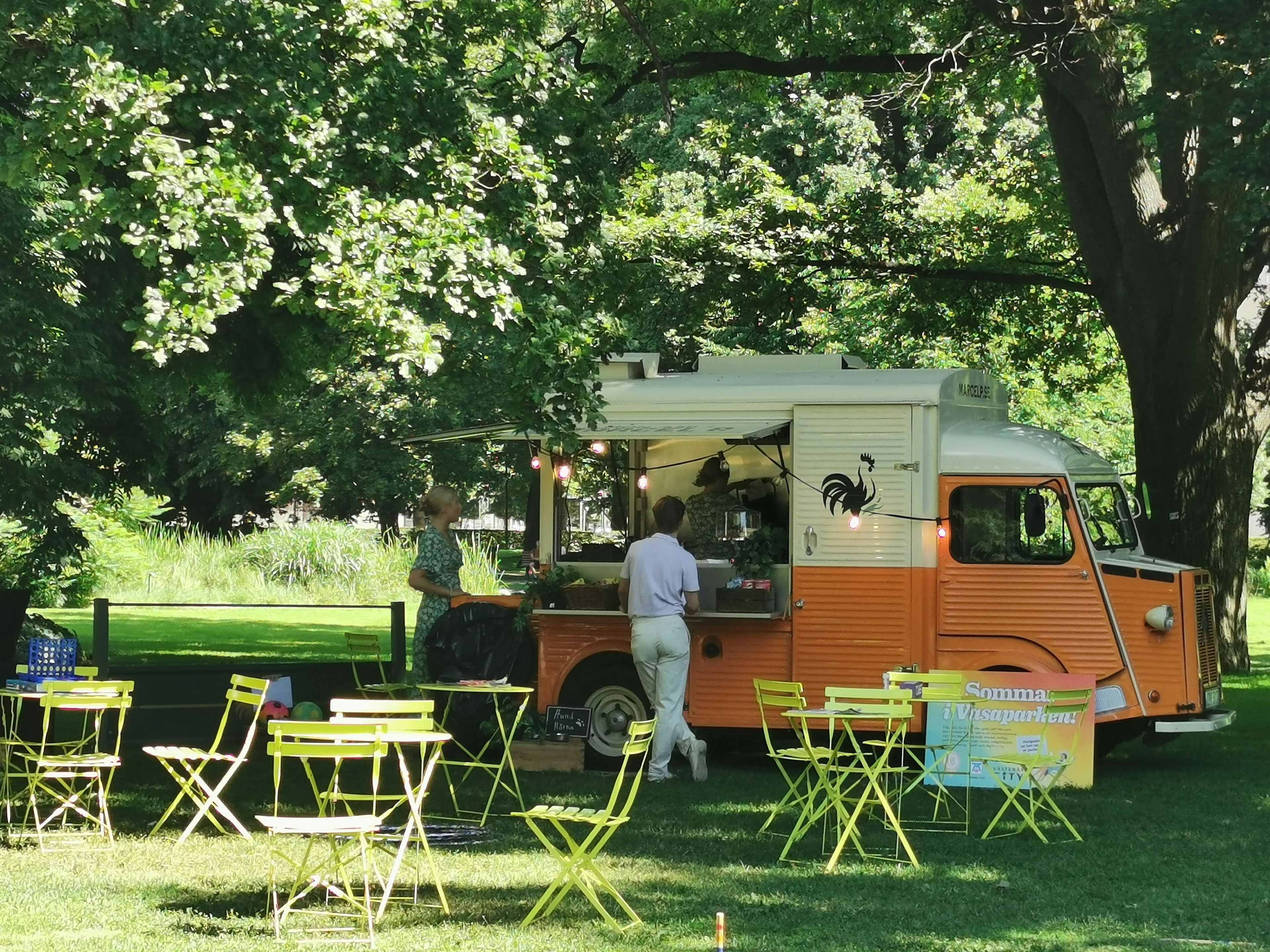 Camión de comida naranja en un parque verde con sillas amarillas