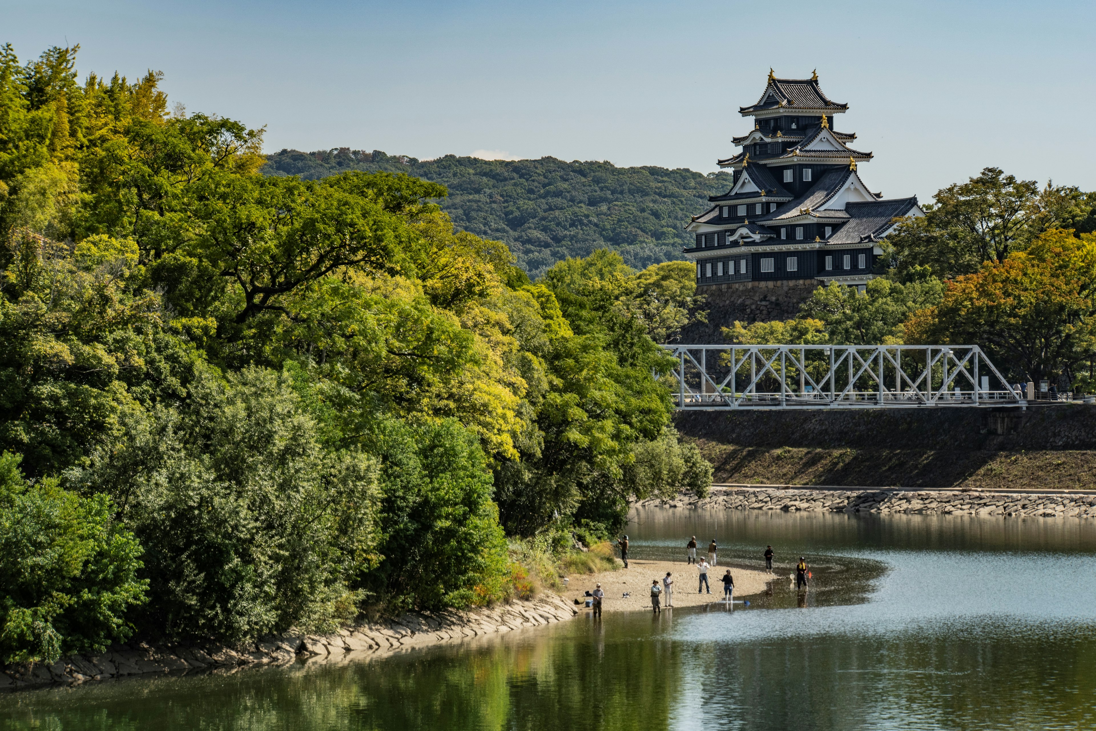 A black castle surrounded by lush greenery and a serene river