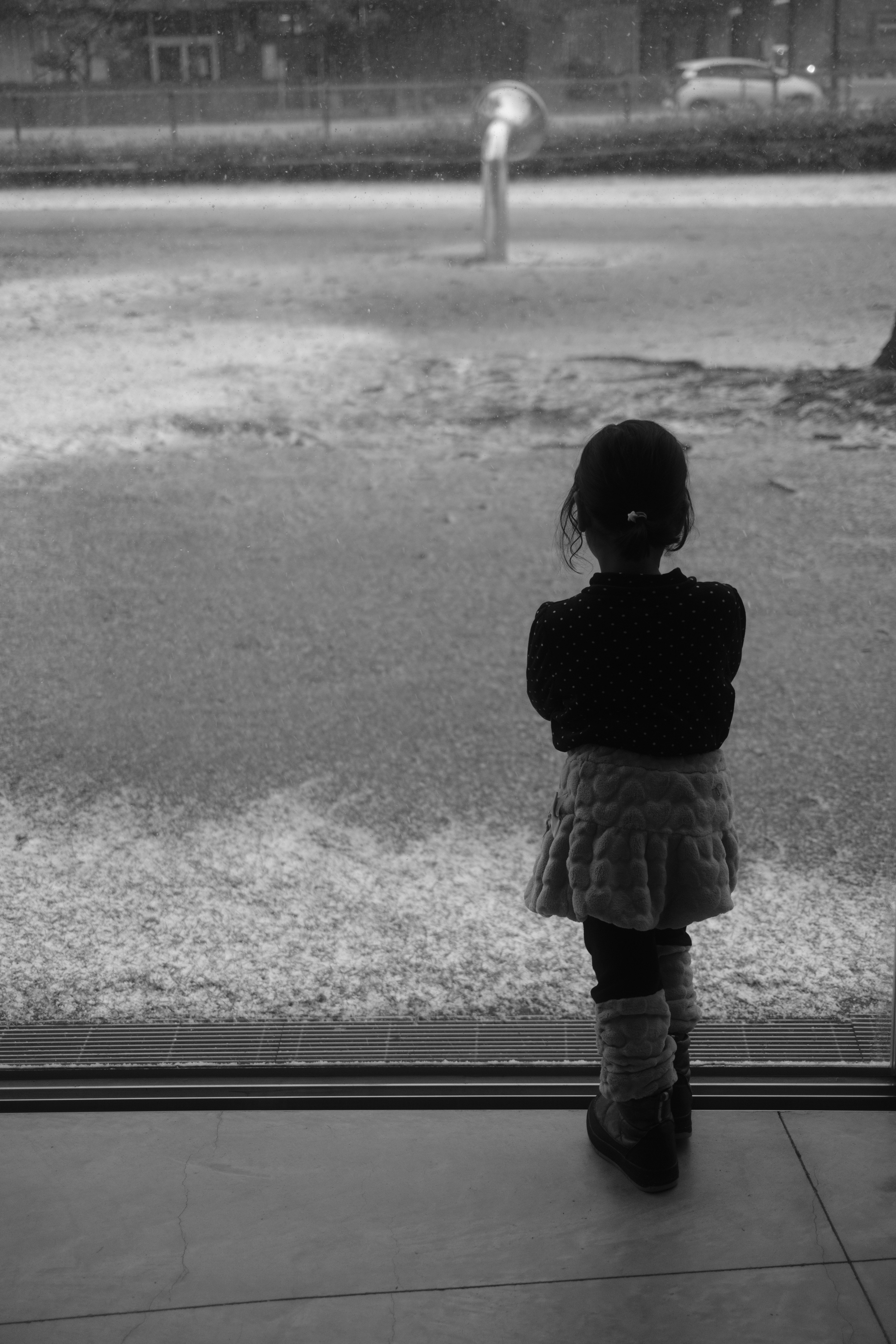 Foto en blanco y negro de un niño de pie junto a una ventana mirando hacia afuera