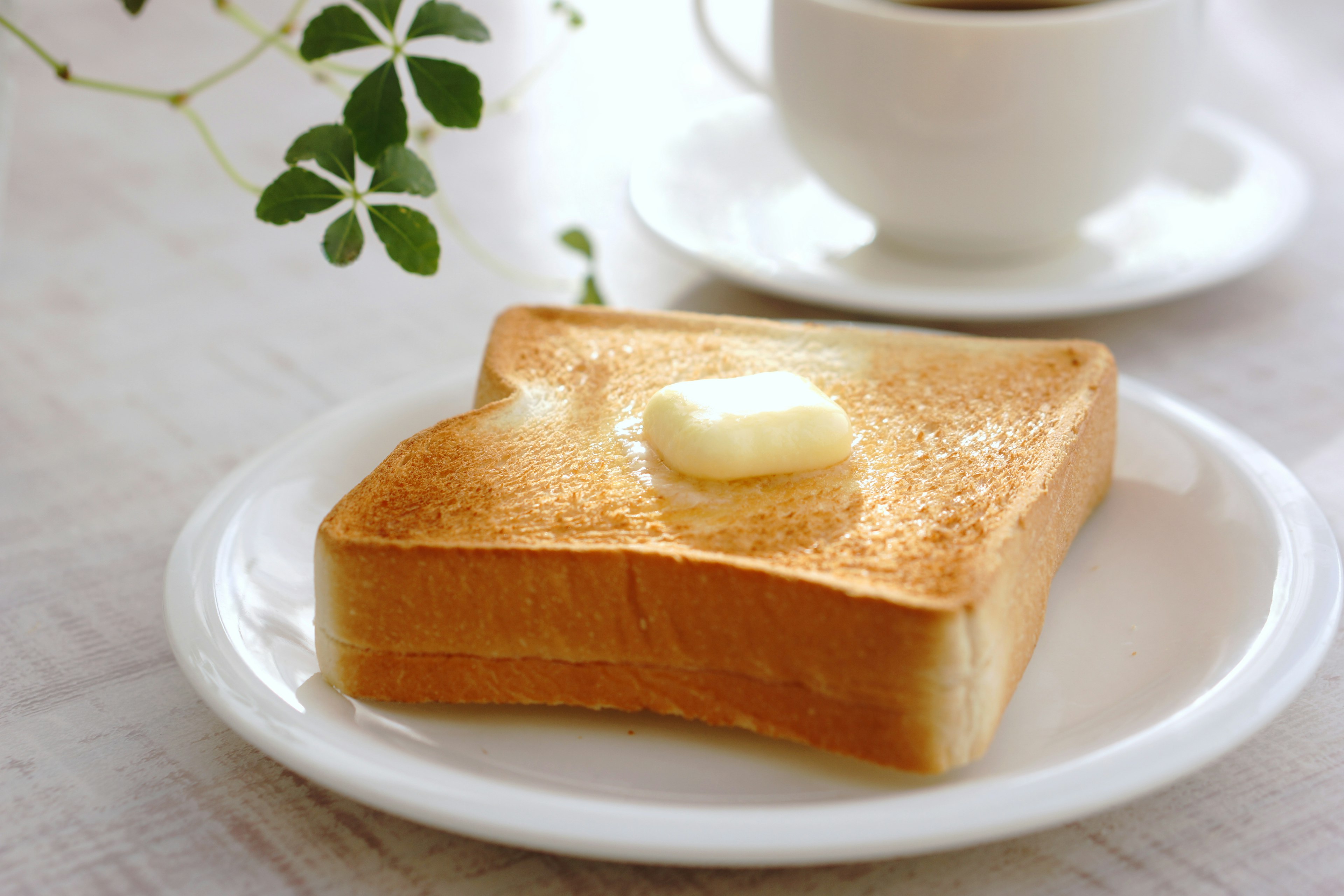 Une tranche de pain grillé avec du beurre sur une assiette blanche accompagnée d'une tasse de café