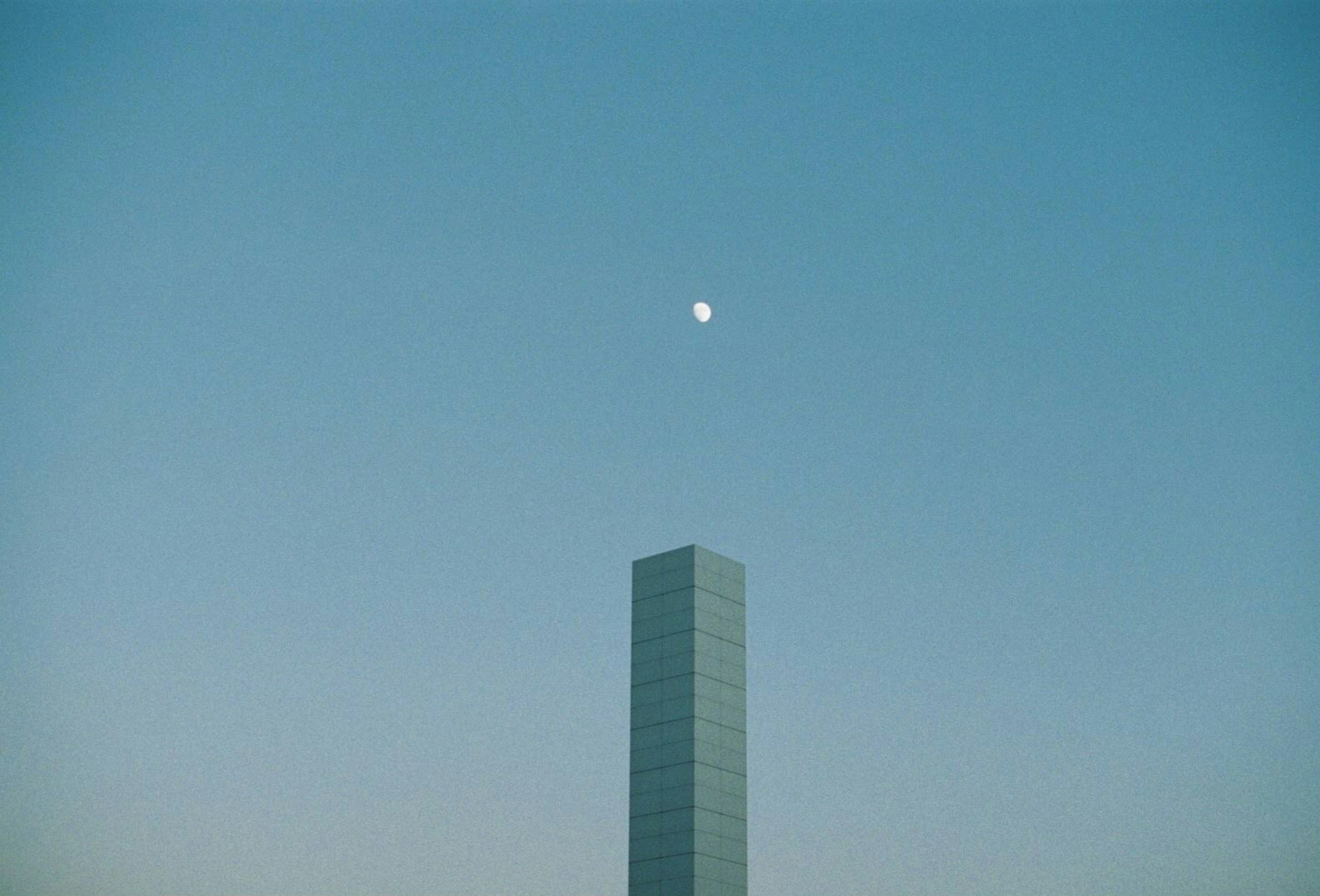 Silhouette di un alto edificio contro un cielo blu con una luna visibile