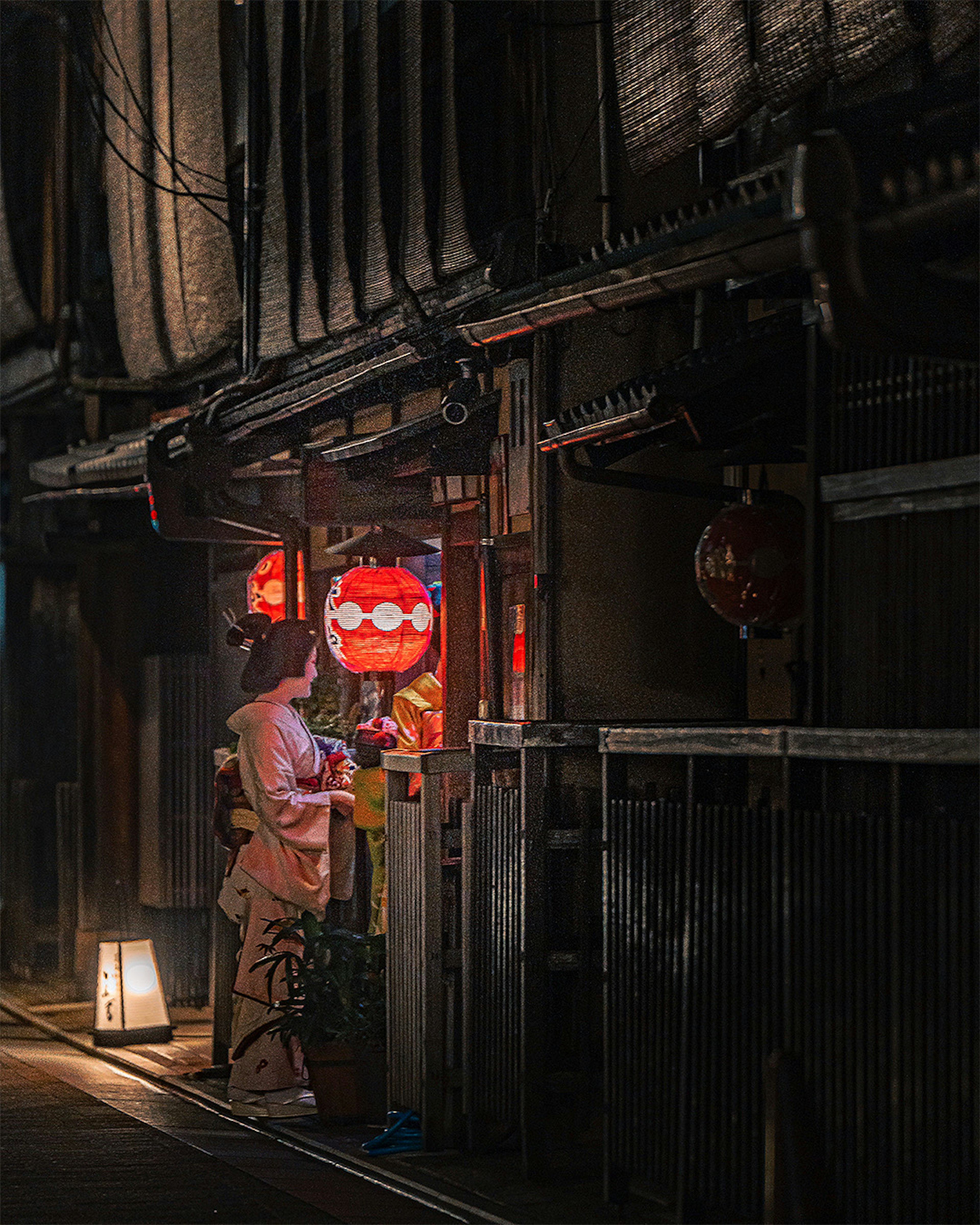 Escena nocturna en un callejón japonés con faroles rojos iluminando a una mujer frente a una tienda